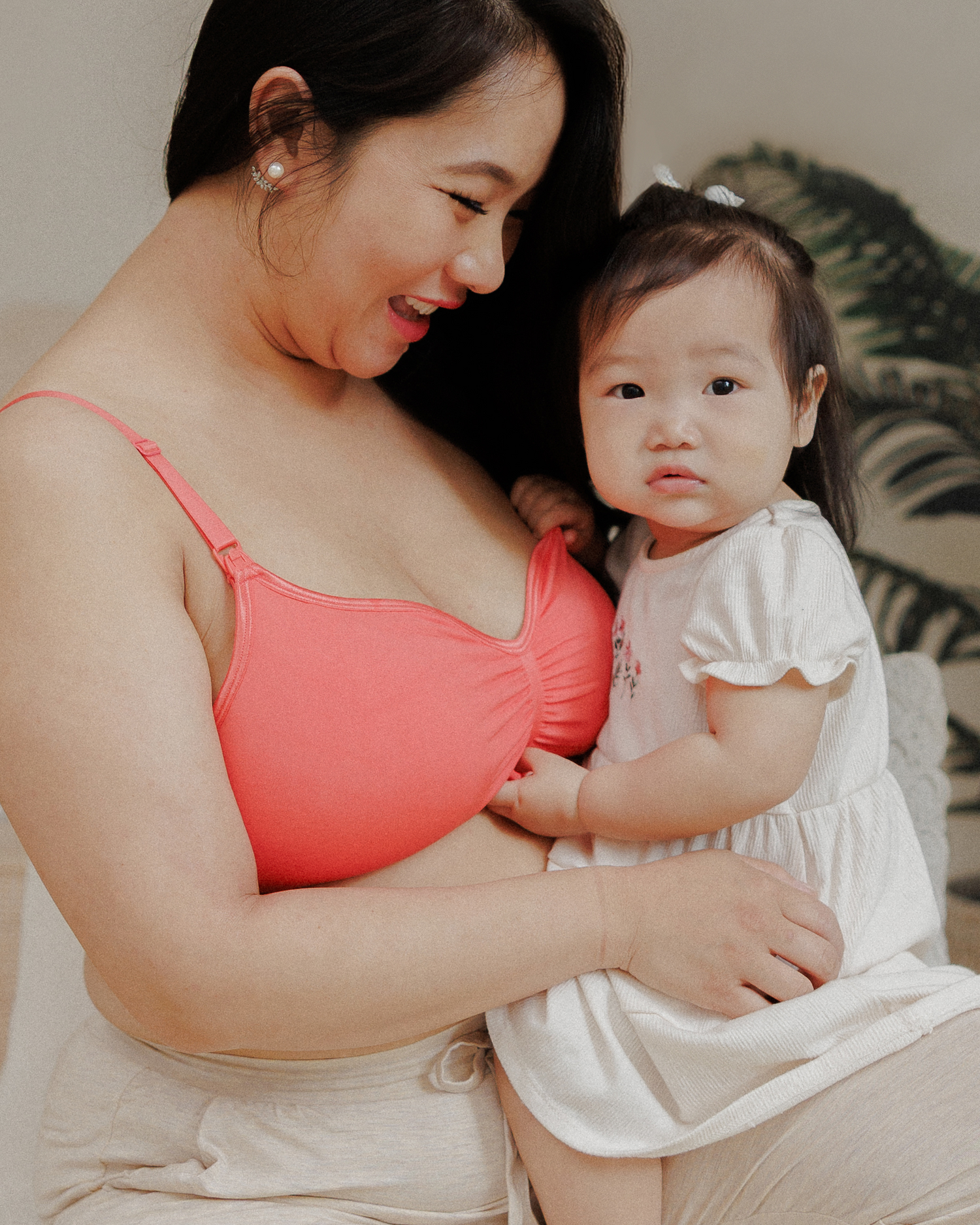 Model wearing the Tatum Seamless Maternity & Nursing Bralette in Coral Sunset, and smiling down at daughter