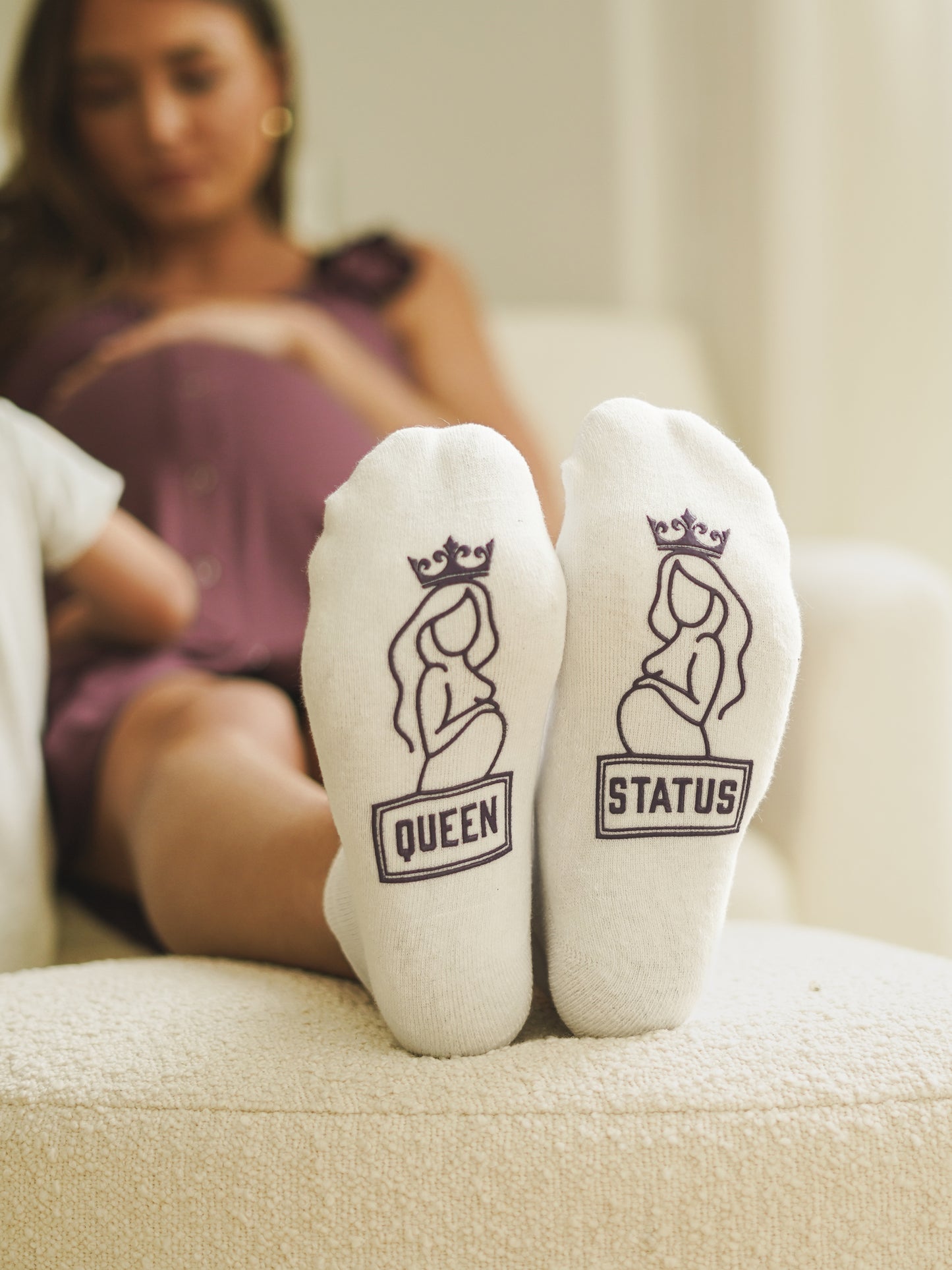 Model sitting on chair with feet on ottoman wearing Queen Status Labor & Delivery Socks