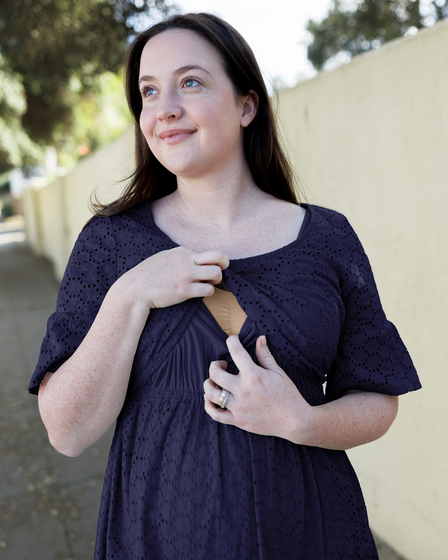 Close up of model wearing the Dahlia Eyelet Maternity & Nursing Dress in Navy, lifting top outer layer to show nursing access