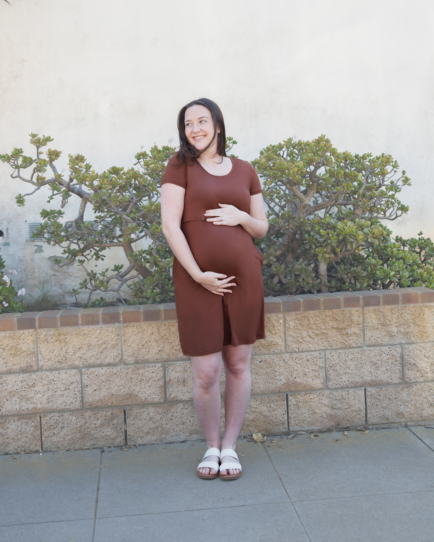 Front view of pregnant model outside wearing the Eleanora Bamboo Maternity & Nursing Dress in Redwood, paired with sandals