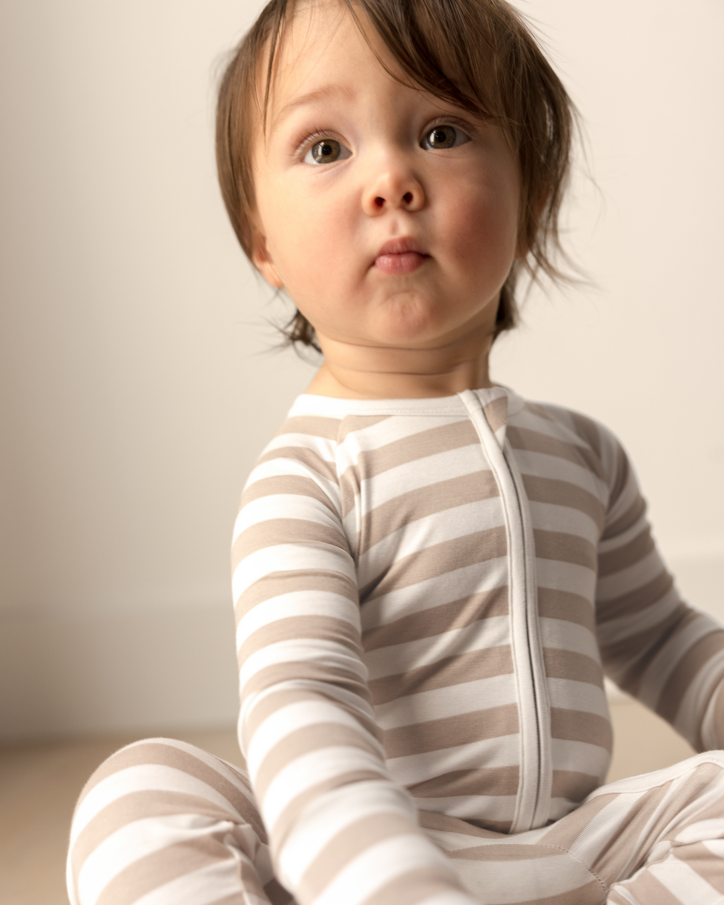 Child wearing Bamboo Baby Pajamas in Fawn Stripe sitting on a light-colored floor.