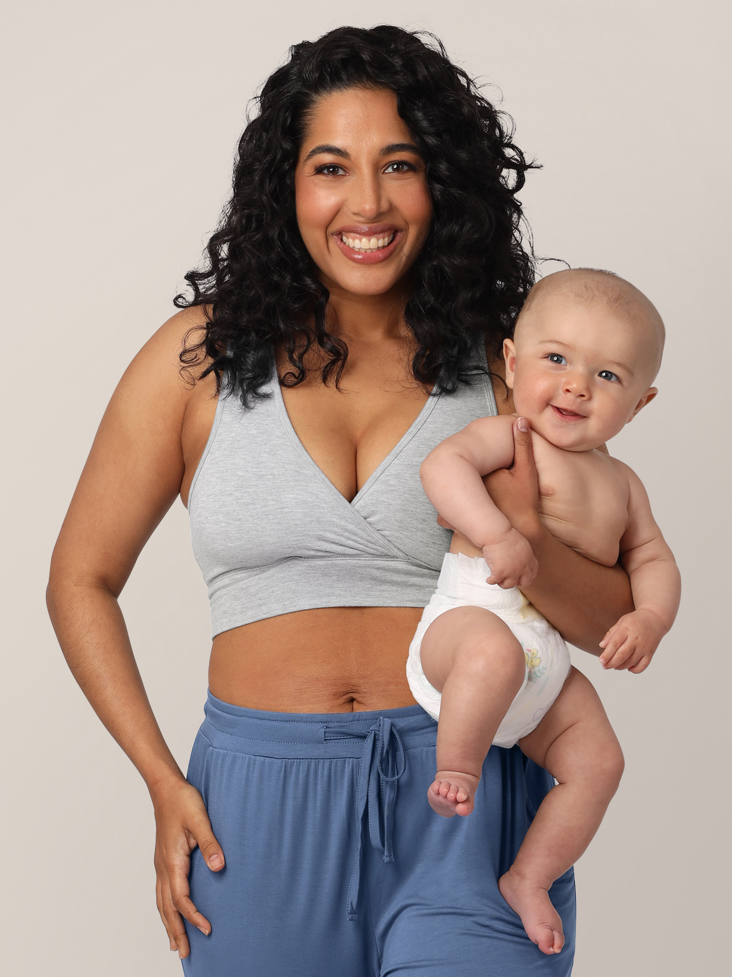 Model wearing the French Terry Nursing Bra in Grey Heather and the Everyday Joggers in Slate Blue. She is holding her smiling infant. @model_info:Zakeeya is wearing a Small.