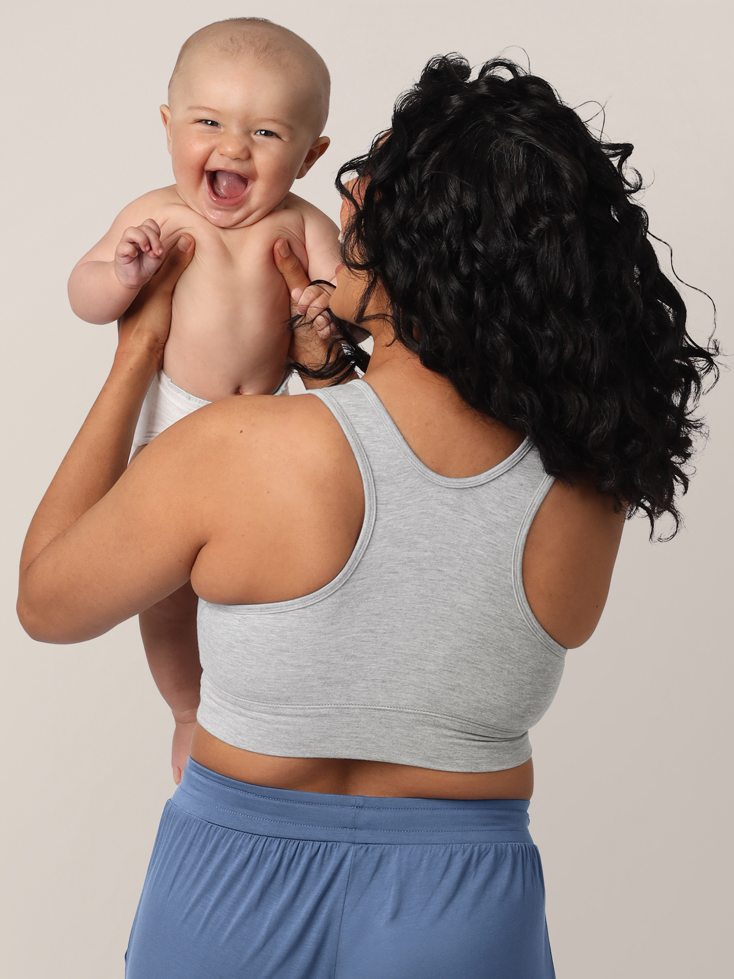 Model showing the racerback detail of the French Terry Nursing Bra in grey while holding her smiling baby.