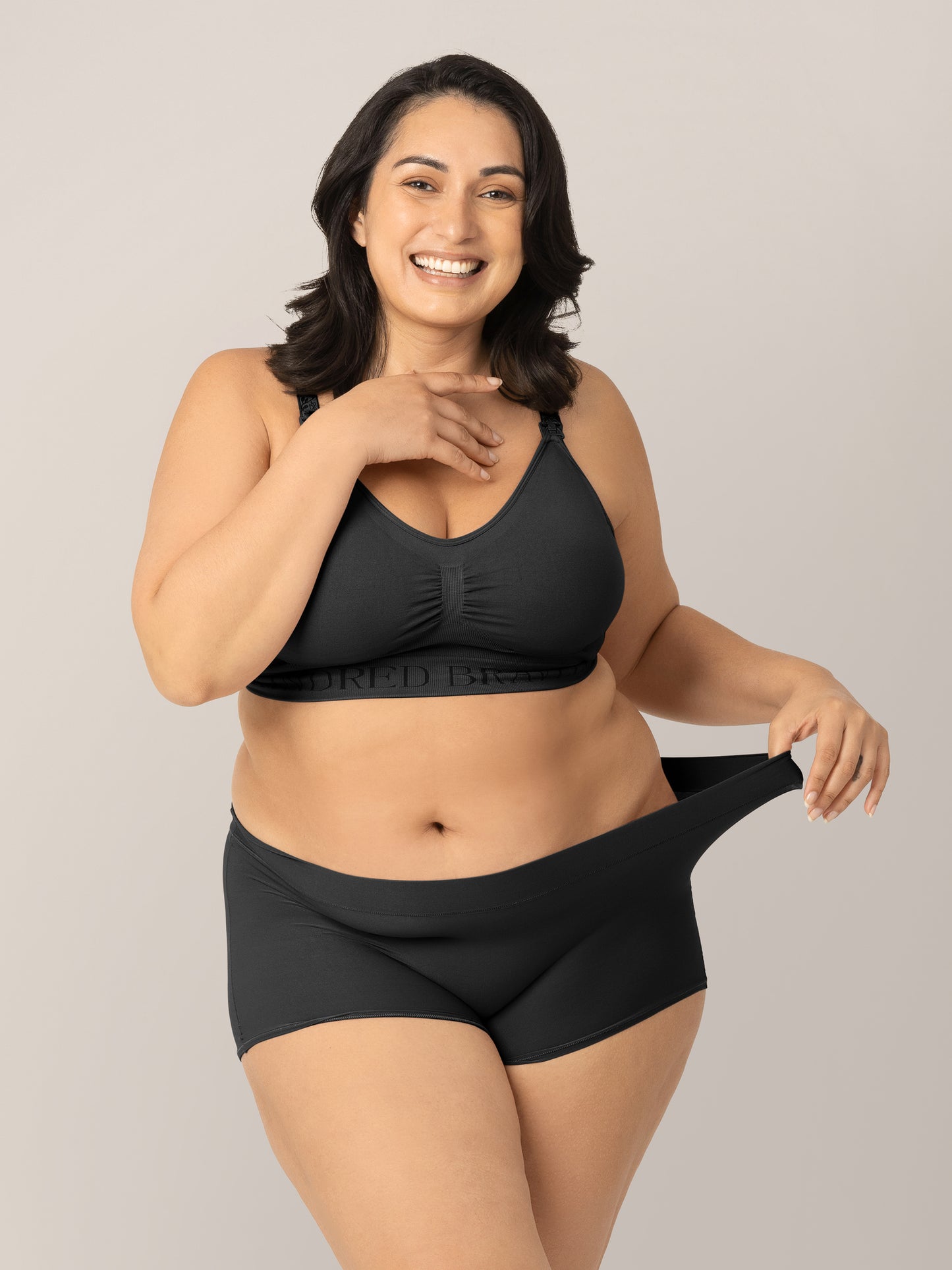 Model wearing the Black Grow with Me™ Maternity & Postpartum Boyshort and pulling the waistband to show stretch. @model_info: Connie is wearing an X-Large.