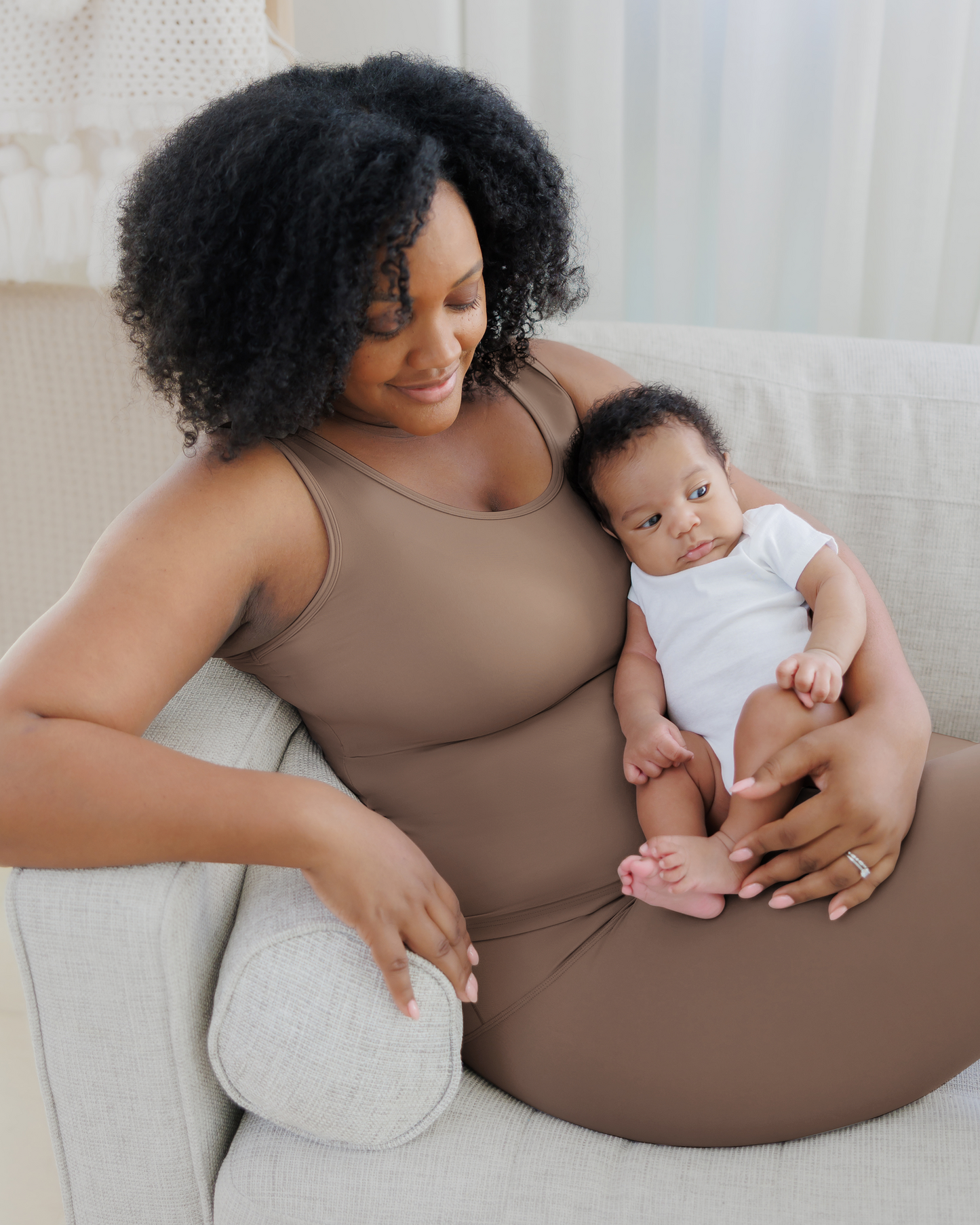 Model on sofa cradling baby, wearing the Grow with Me™ Maternity & Nursing Tank in Taupe paired with matching Grow with Me™ Maternity & Postpartum Legging @model_info:Roxanne is wearing a Large.