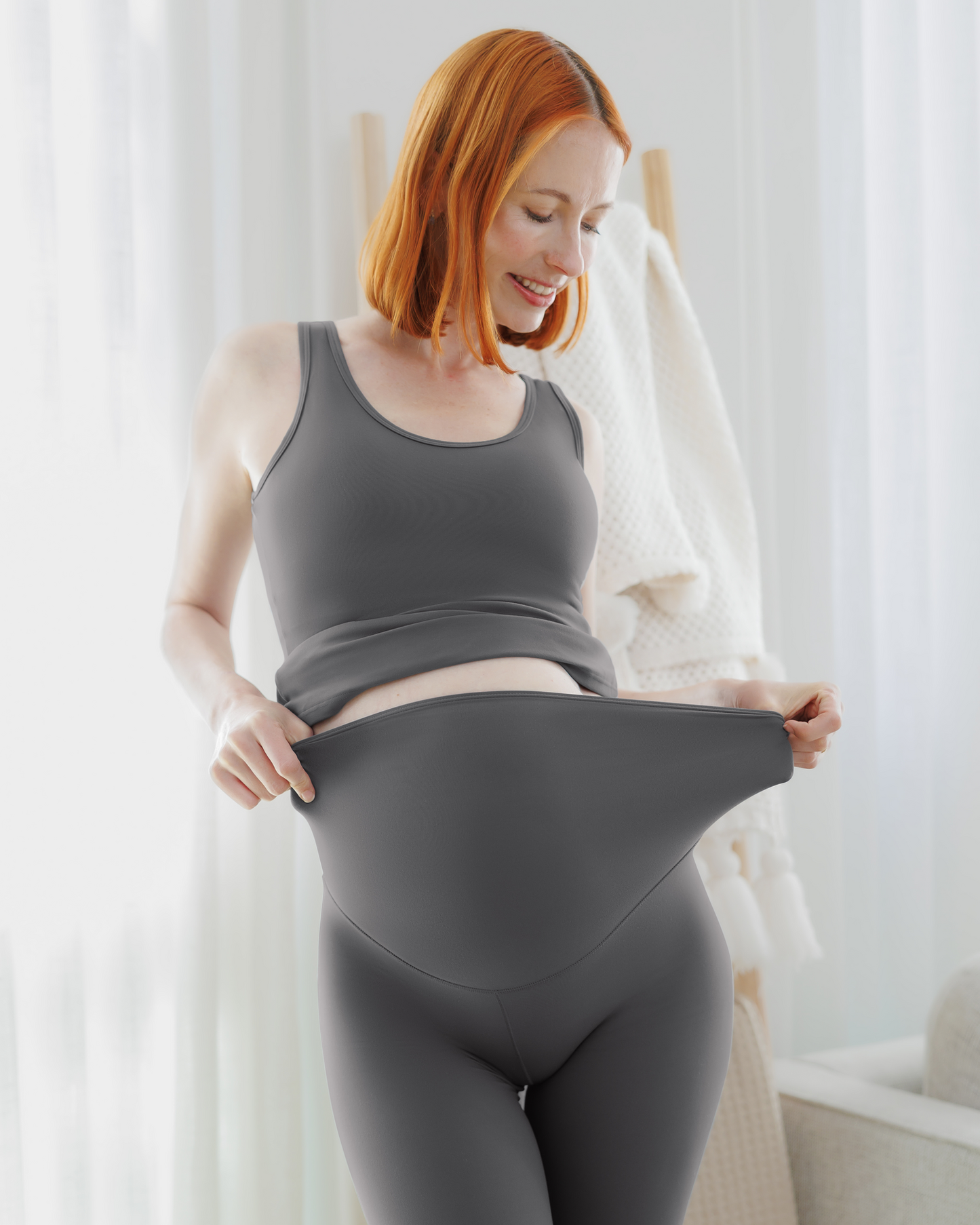 Pregnant model leaning on chair wearing the Grow with Me™ Maternity & Nursing Tank in Stormy Grey, paired with matching Grow with Me™ Maternity & Postpartum Legging @model_info:Anna is wearing a Small.