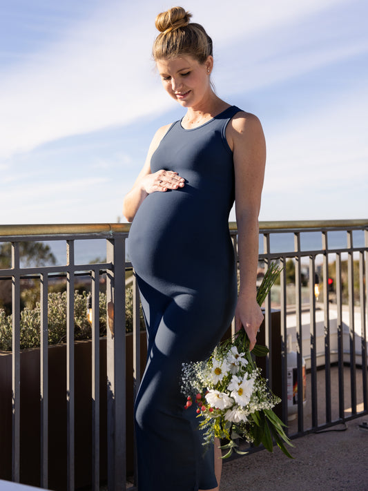 Outside picture of a pregnant model wearing the Gwen Ribbed Bamboo Maternity Midi Dress in Navy.@model_info:Amber is wearing a Small. 