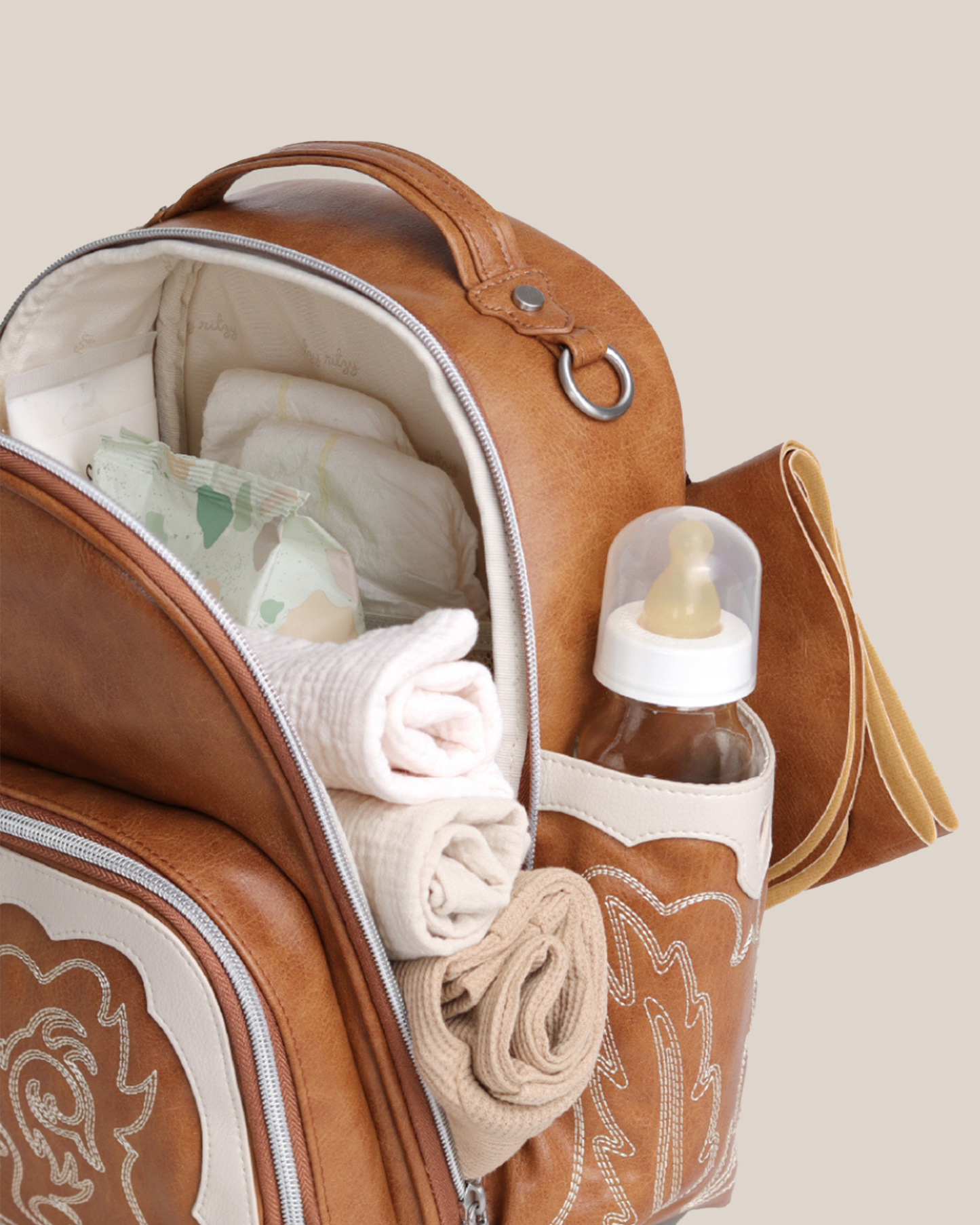 Close up of the Itzy Ritzy - Nash Itzy Mini Plus™ Diaper Bag in Saddle showing what can be carried in it