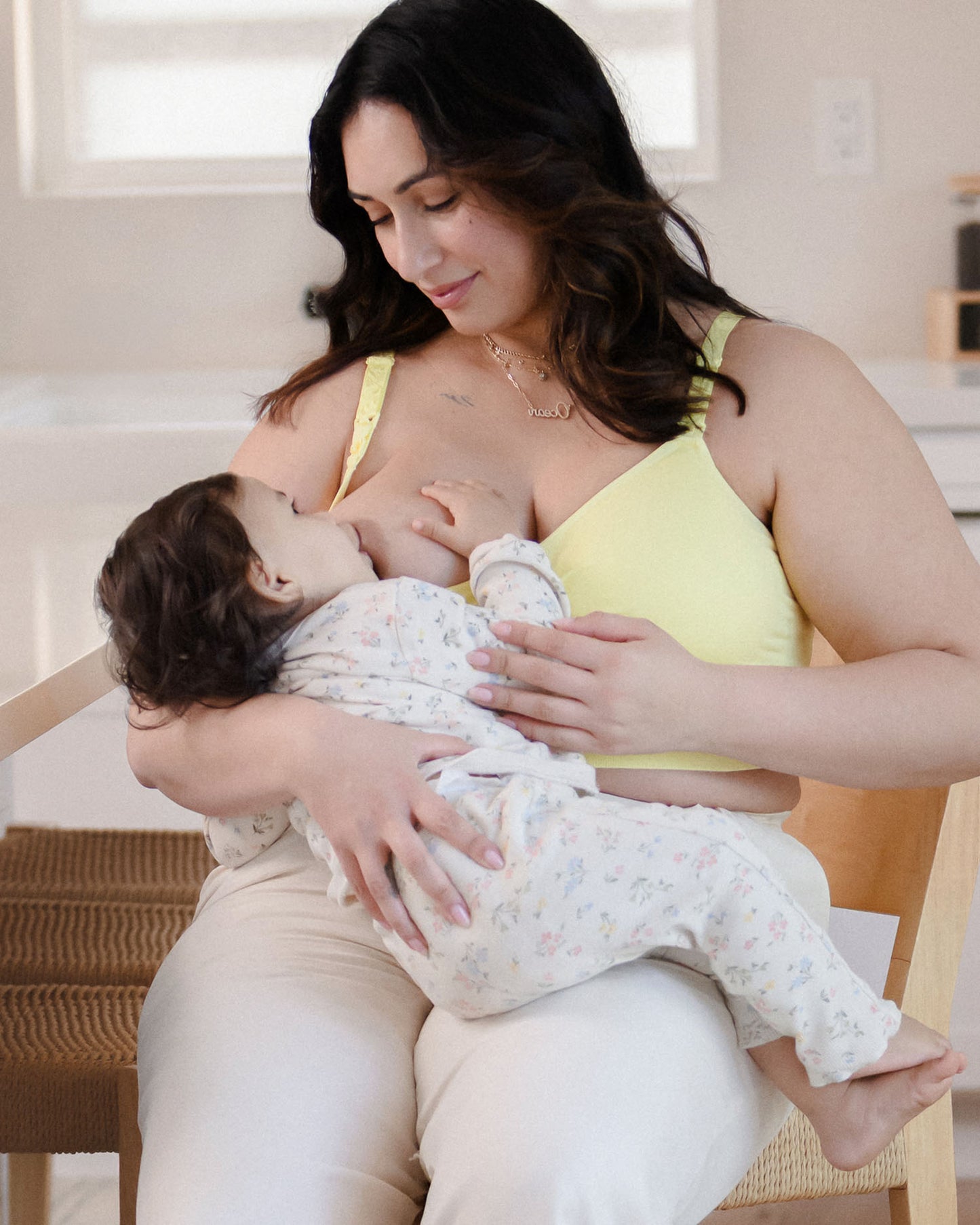 Model sitting in kitchen nursing baby and wearing the Sublime® Hands-Free Pumping & Nursing Bra Light Lemon @model_info:Connie is wearing an X-Large Busty.