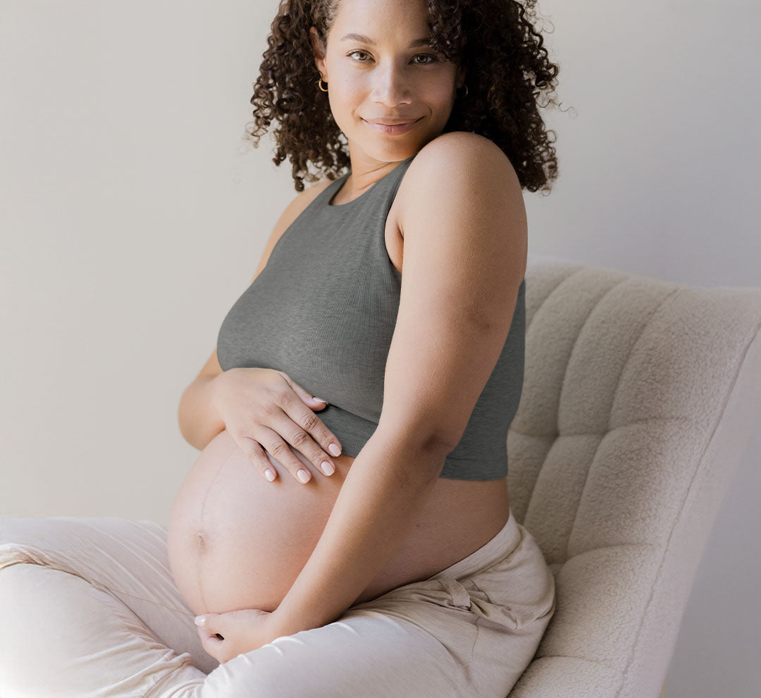 Front 3/4 view of pregnant model sitting in chair and wearing the Sublime® Bamboo Maternity & Nursing Longline Bra in Charcoal