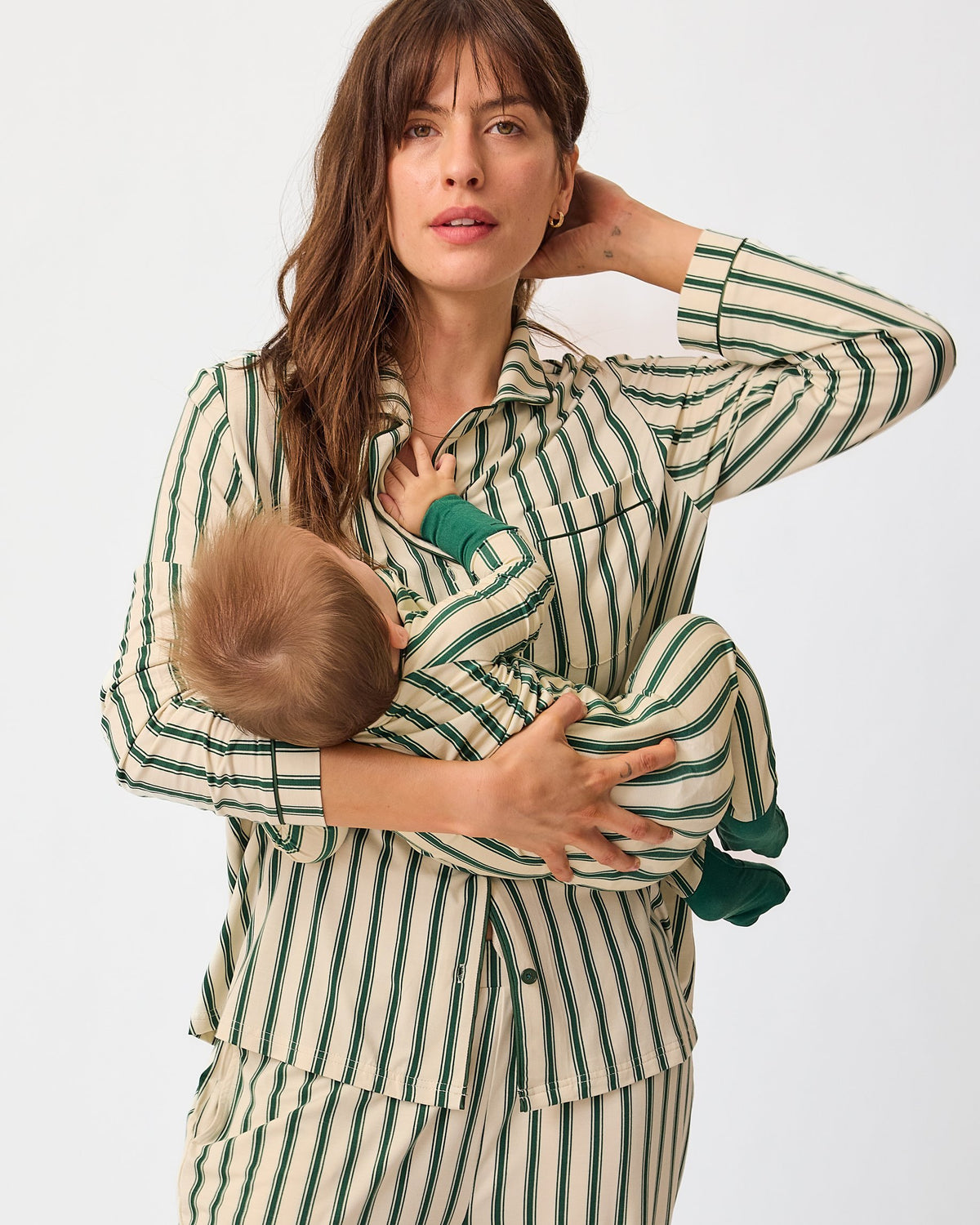 Mother and baby are wearing matching pajamas, mother wears Clea Bamboo Long Sleeve Pajama Set in Green Candy Stripe and baby wears Bamboo Baby Pajama in Green Candy Stripe, on an off white background.