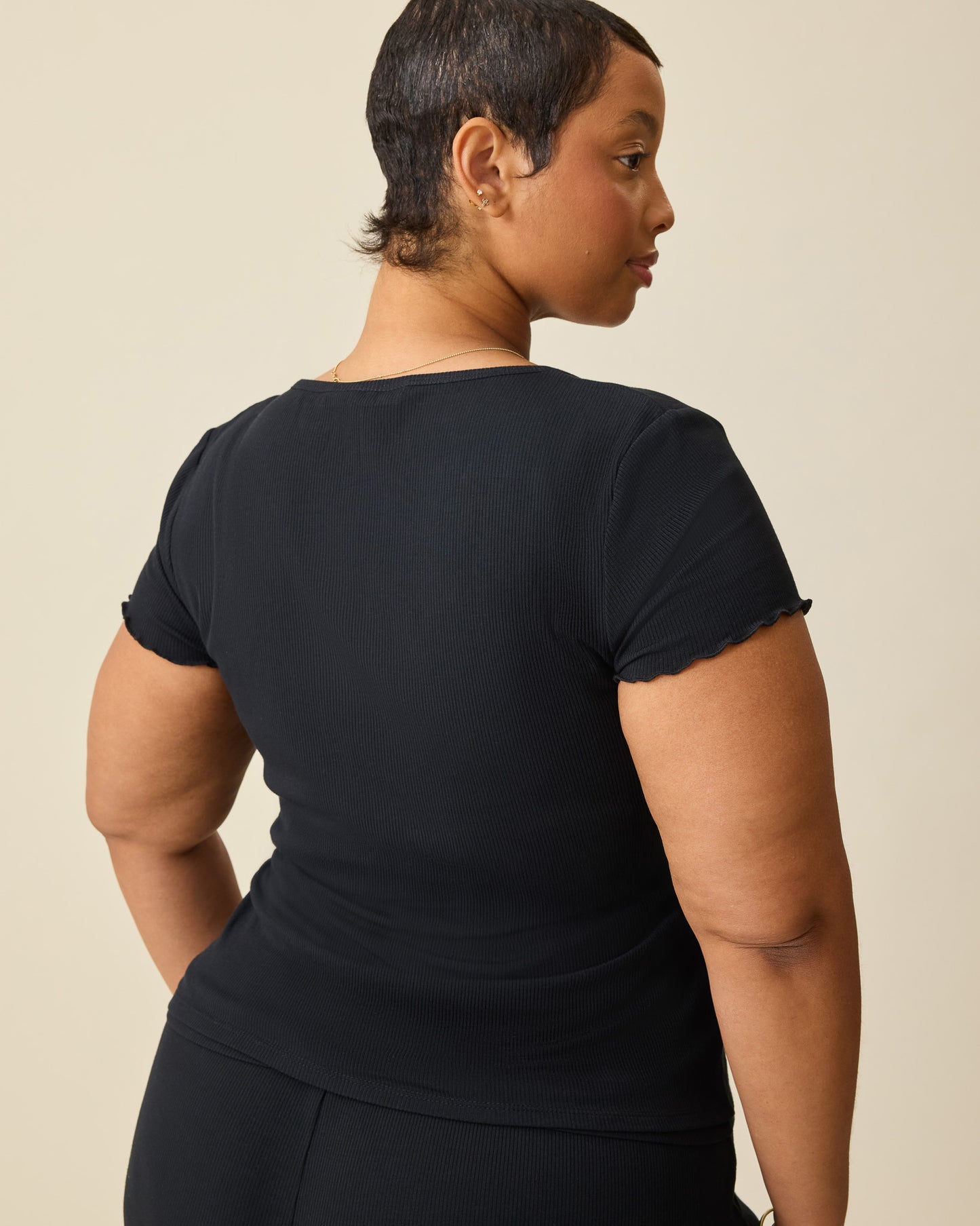 Back view of model wearing Ribbed Modal Notched Nursing T-shirt in Black on a beige background.
