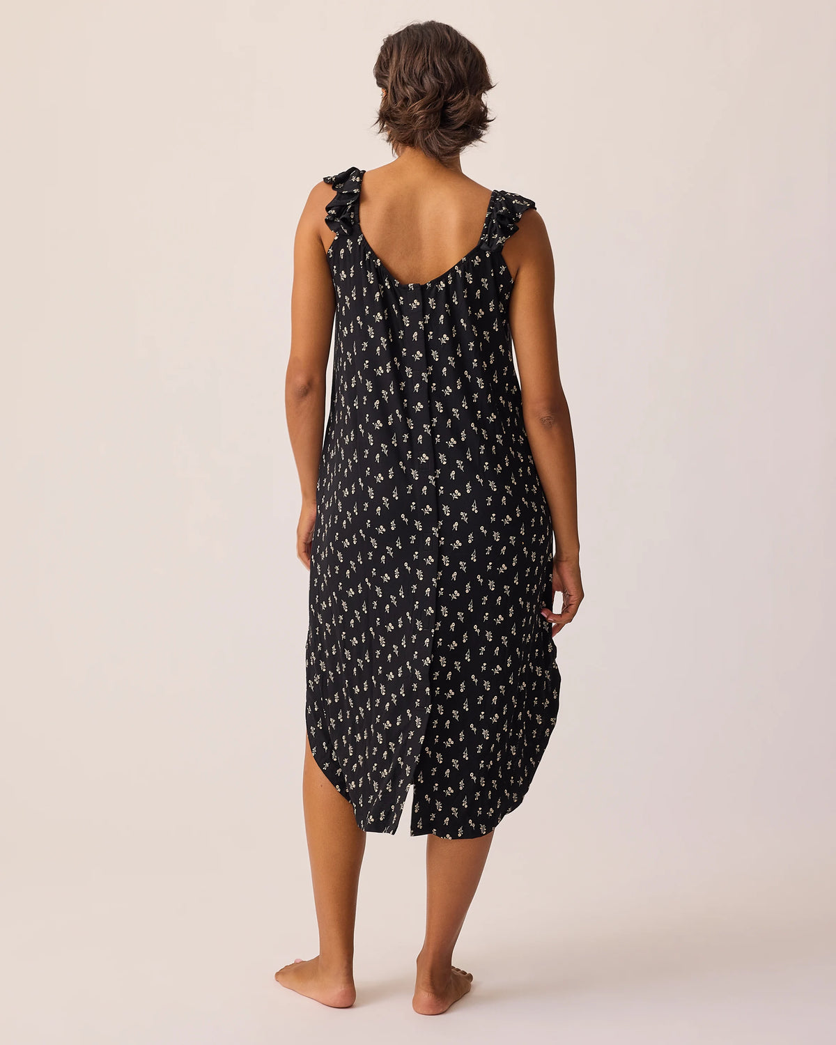 Back view of model wearing Ruffle Strap Labor & Delivery Gown in Black Wildflower on a beige background.