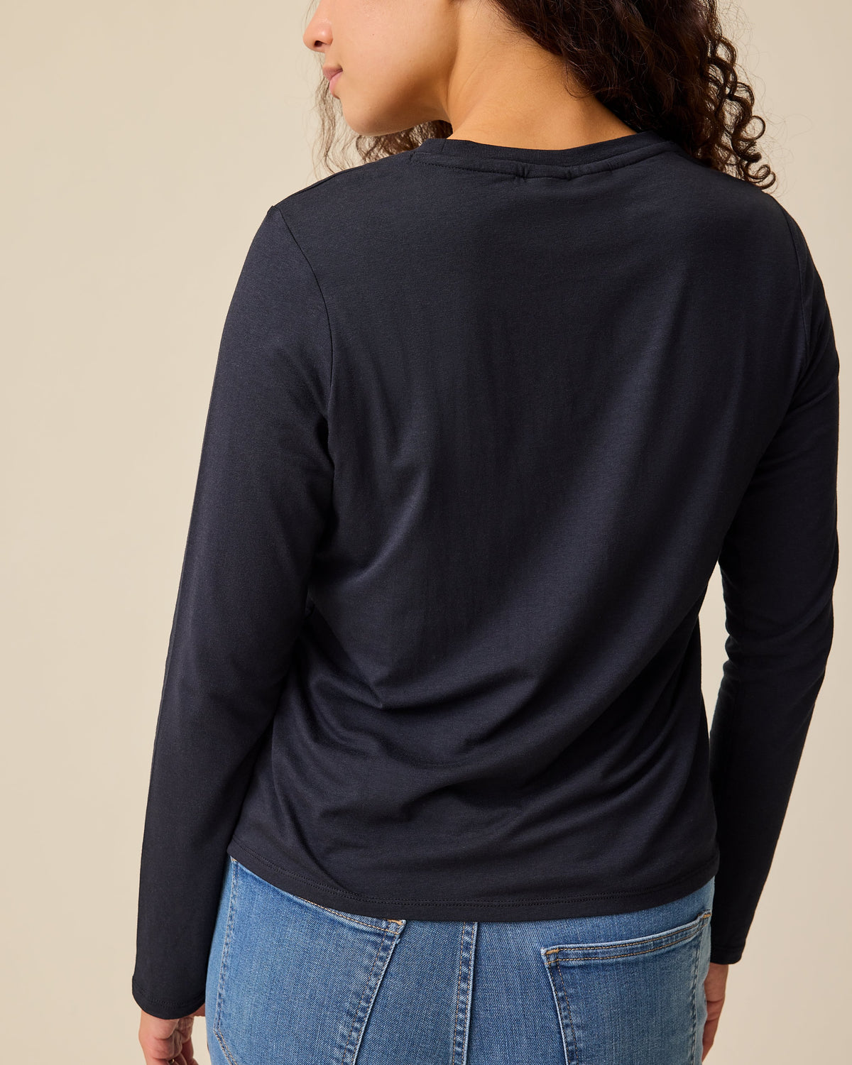 Back view of model wearing Modal Long Sleeve Nursing T-shirt in Black and Wide Leg Maternity & Postpartum Jean in Medium Wash on a beige background.