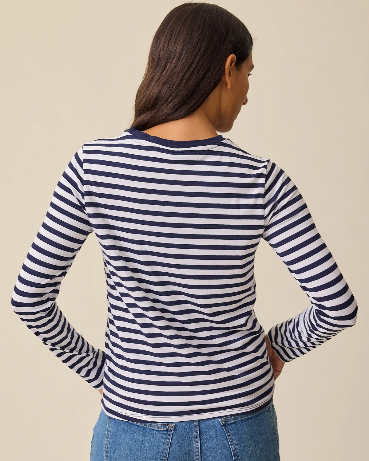 Back view of model wearing Modal Long Sleeve Nursing T-shirt in Navy & White Stripe and Wide Leg Maternity & Postpartum Jean in Medium Wash on a beige background.