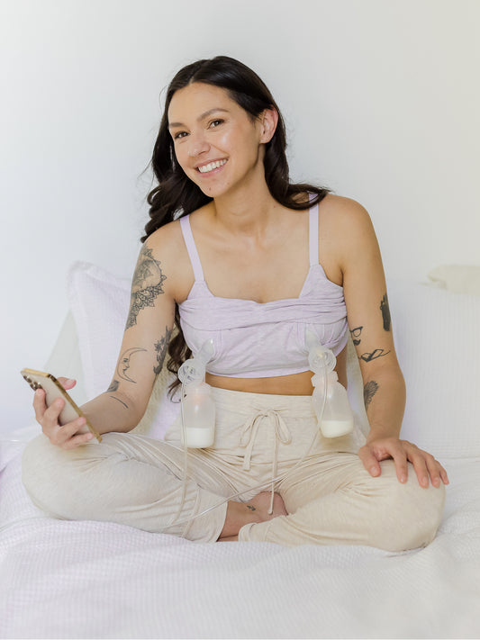 Model sitting cross-legged on bed and pumping, wearing the Sublime® Bamboo Hands-Free Pumping Lounge & Sleep Bra in Lavender Heather @model_info:Megan is wearing a Small.