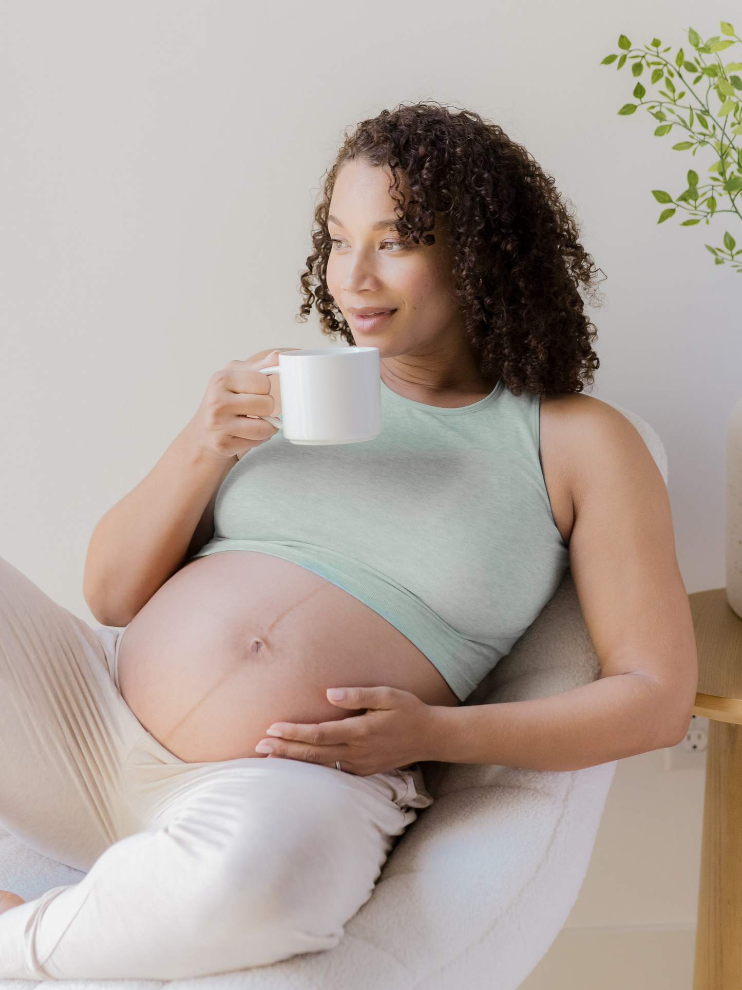 Pregnant model lounging holding mug and wearing the Sublime® Bamboo Maternity & Nursing Longline Bra in dusty blue green heather.