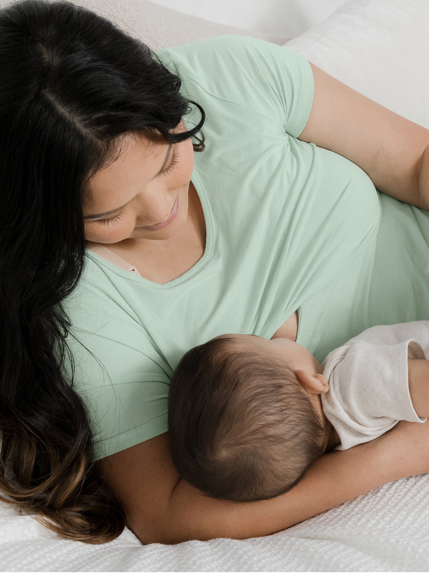 Model laying down while breastfeeding her baby through the convenient nursing panel on the Eleanora Bamboo Maternity & Nursing Dress in Soft Mint.