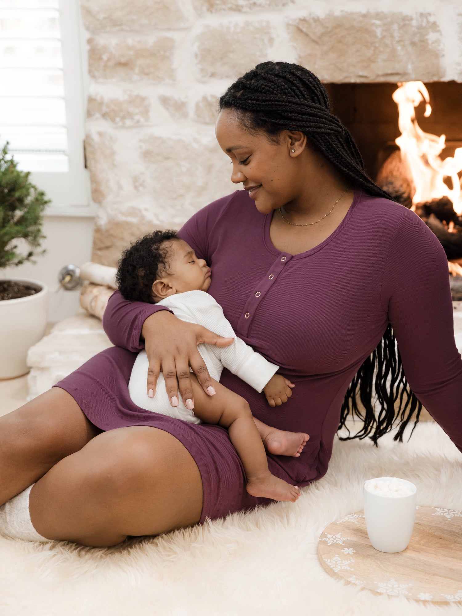 Model wearing the Betsy Ribbed Bamboo Maternity & Nursing Nightgown in Burgundy Plum holding her baby against her chest. @model_info:Roxanne is wearing a Large.