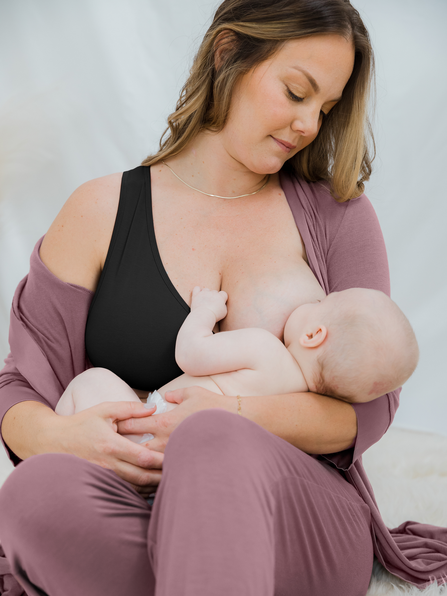 Model breastfeeding her infant while wearing the French Terry Nursing Bra in Black, the Emmaline Robe in Twilight and the Everyday Joggers in Twilight. 