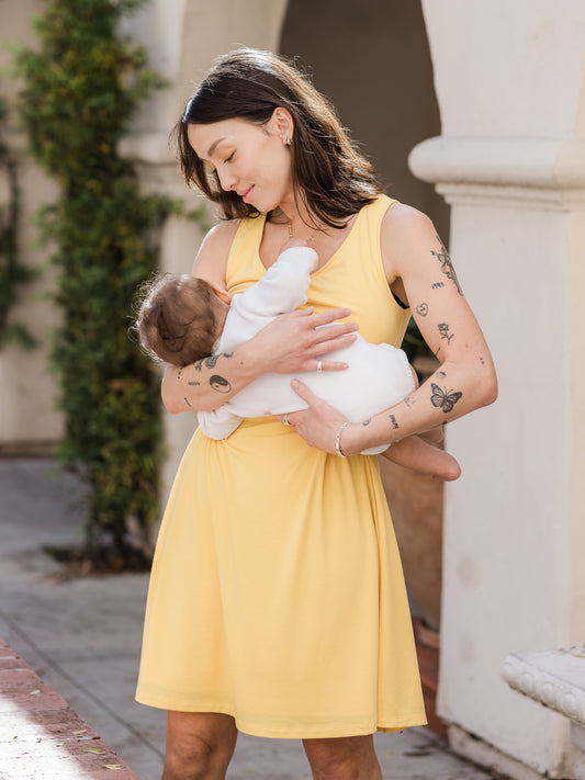 Front view of model wearing the Penelope Crossover Nursing Dress in citrus, standing and nursing baby @model_info:Lyn is wearing a Small.