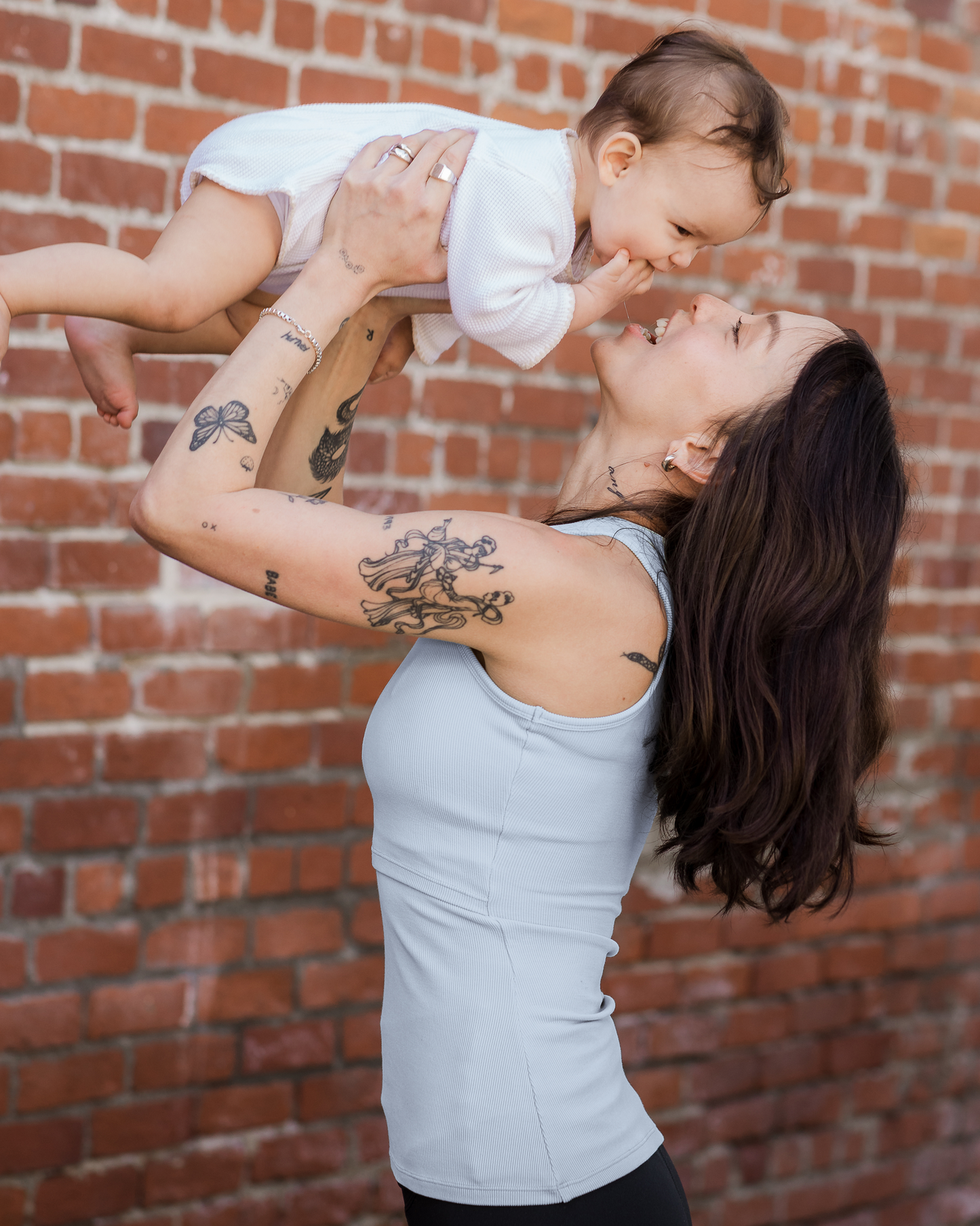 Side view of model outside wearing the Ribbed Bamboo Racerback Nursing Tank in French Blue, lifting baby up overhead