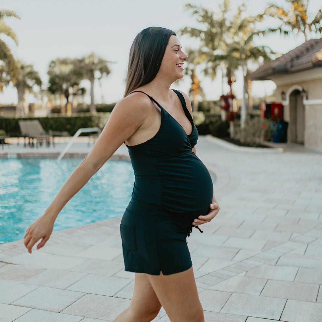 Pregnant model wearing the Maternity & Postpartum Swim Short in Black walking by the pool. @model_info:Alyssa is wearing a Medium.