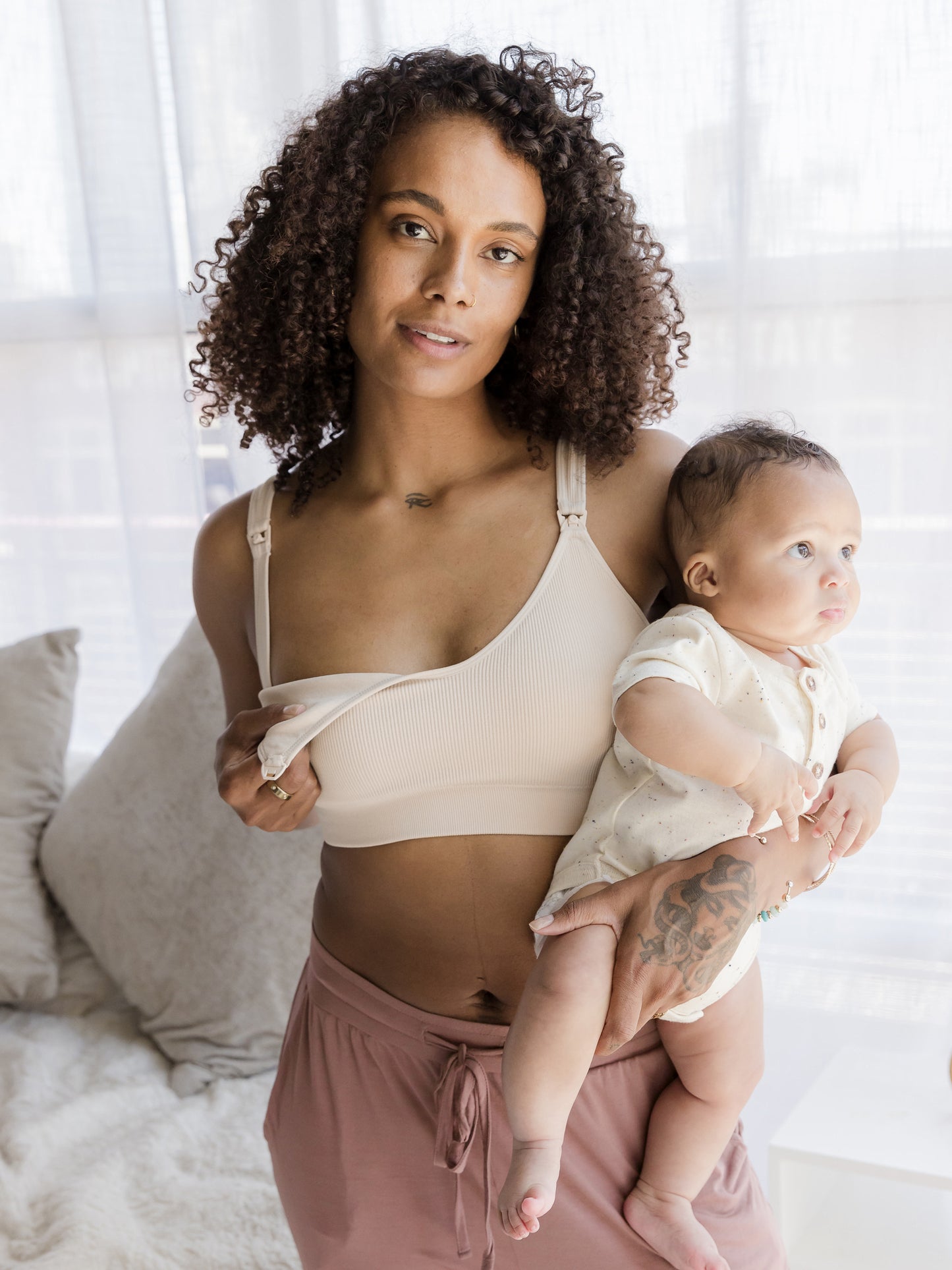 Model holding baby, wearing the Mia Maternity & Nursing Lounge Bra in Stone and showing clip down nursing access.