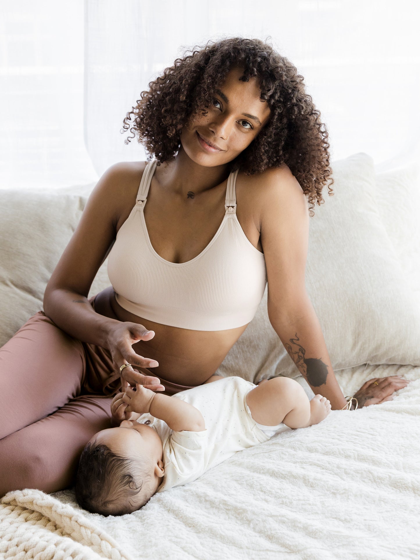 Model sitting on bed with baby and wearing the Mia Maternity & Nursing Lounge Bra in Stone.