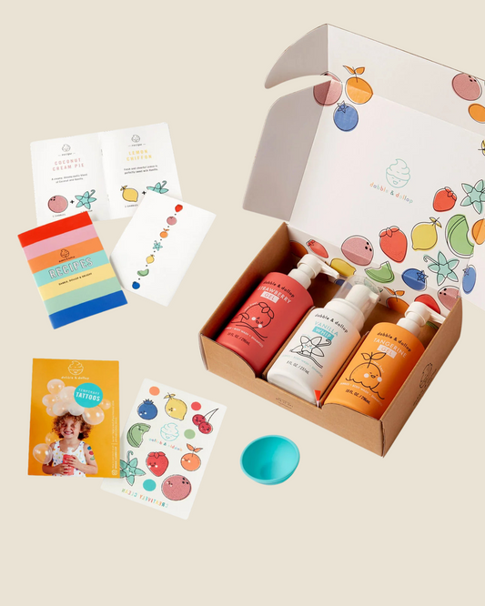 Dabble & Dollop The Original Bubble Bath Bundle product set with bottles, cards, temporary tattoos, and mixing bowl on a beige background