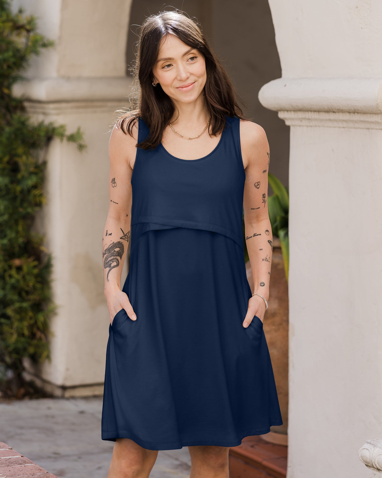 Front view of model outside wearing the Penelope Crossover Nursing Dress in navy, with hands in pockets @model_info:Lyn is 5'6" and wearing a Small.