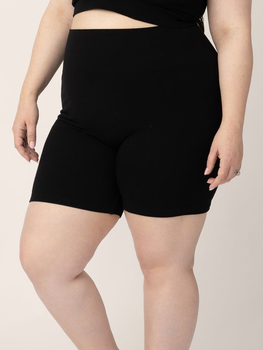 Bottom half of a model wearing the Sublime® Bamboo Maternity & Postpartum Bike Short in Black with her hands at her sides. @model_info:Rachel is 5’6" and wearing a Large.