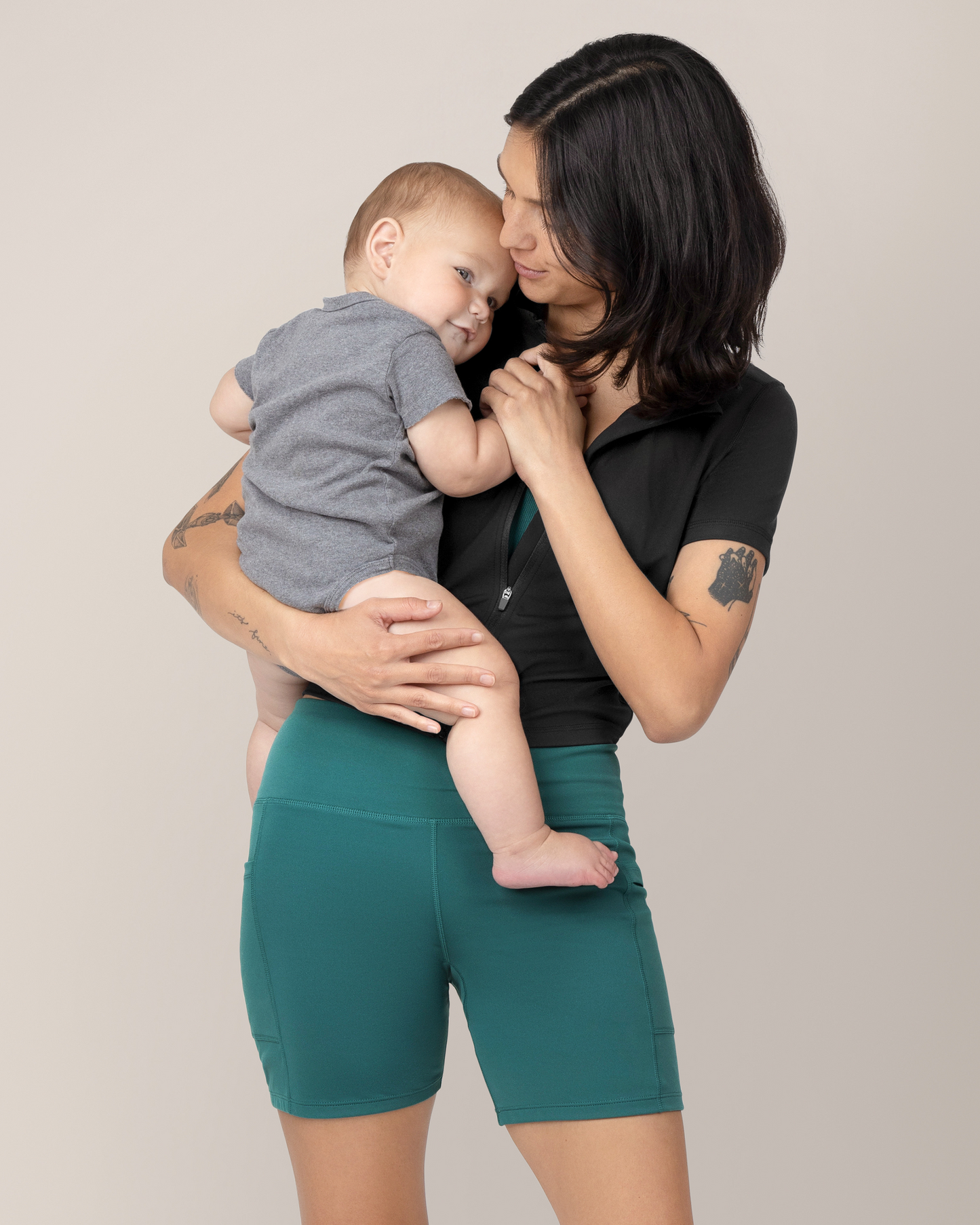 Front view of model holding baby while wearing the Stevie Active Postpartum Bike Short in Teal with the Presley Active Zip Front Nursing Top @model_info:Megan is wearing a Small.