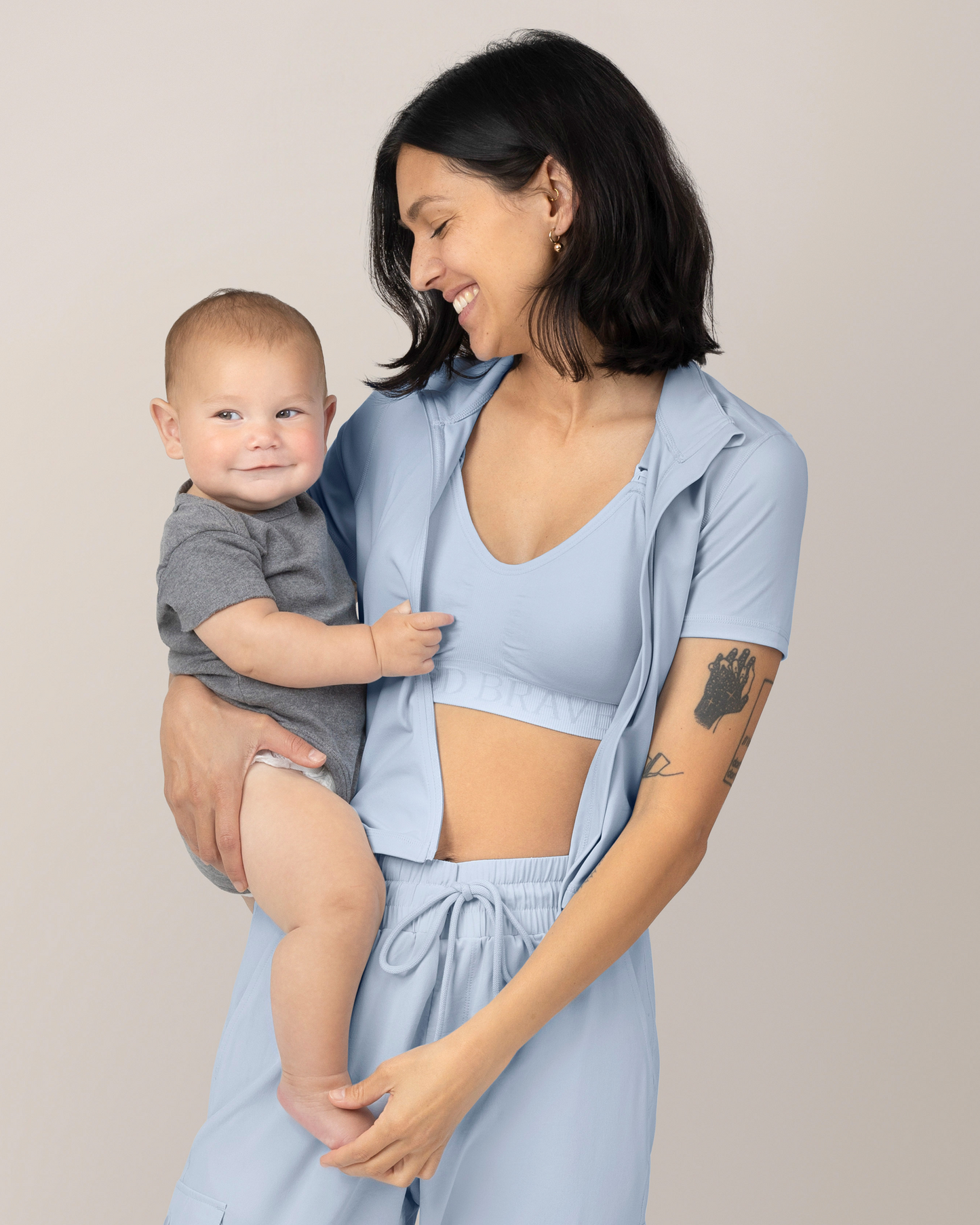 Front view of Model holding baby while wearing the Presley Active Zip Front Nursing Top in Light Blue @model_info:Megan is wearing a Small.