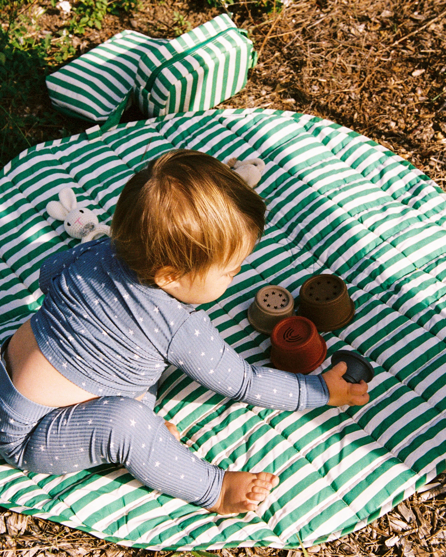 Baby playing on a green and white striped mat outdoors