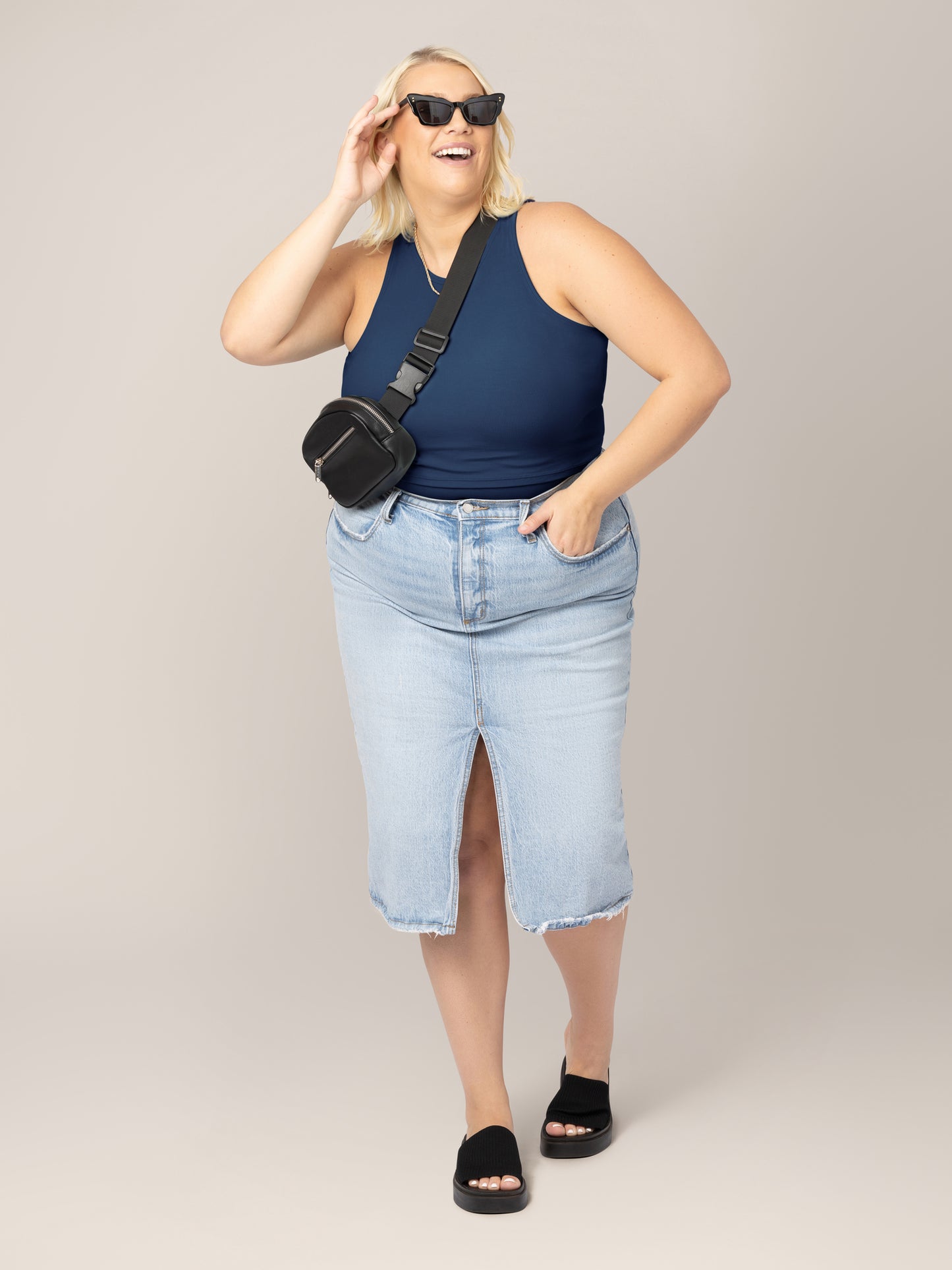 Full body front view of model wearing the Ribbed Bamboo Racerback Nursing Tank in Navy, paired with light denim midi skirt. cross-body belt bag, and sandals