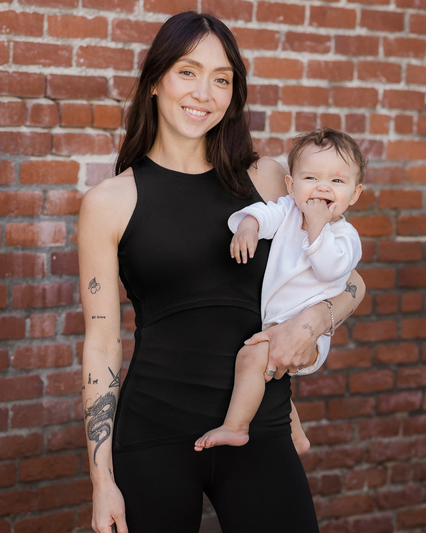 Front view of model holding baby and wearing the Ribbed Bamboo Racerback Nursing Tank in black @model_info:Lyn is wearing a Small.