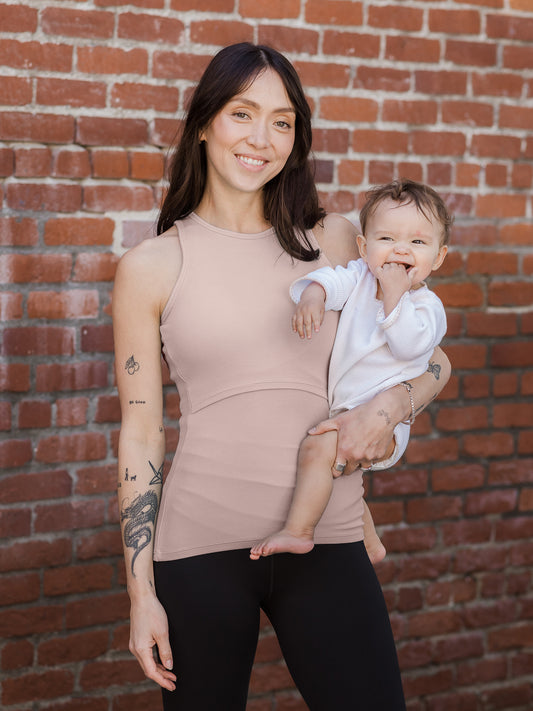 Front view of model wearing the Ribbed Bamboo Racerback Nursing Tank in lilac stone, holding baby @model_info:Lyn is wearing a Small.