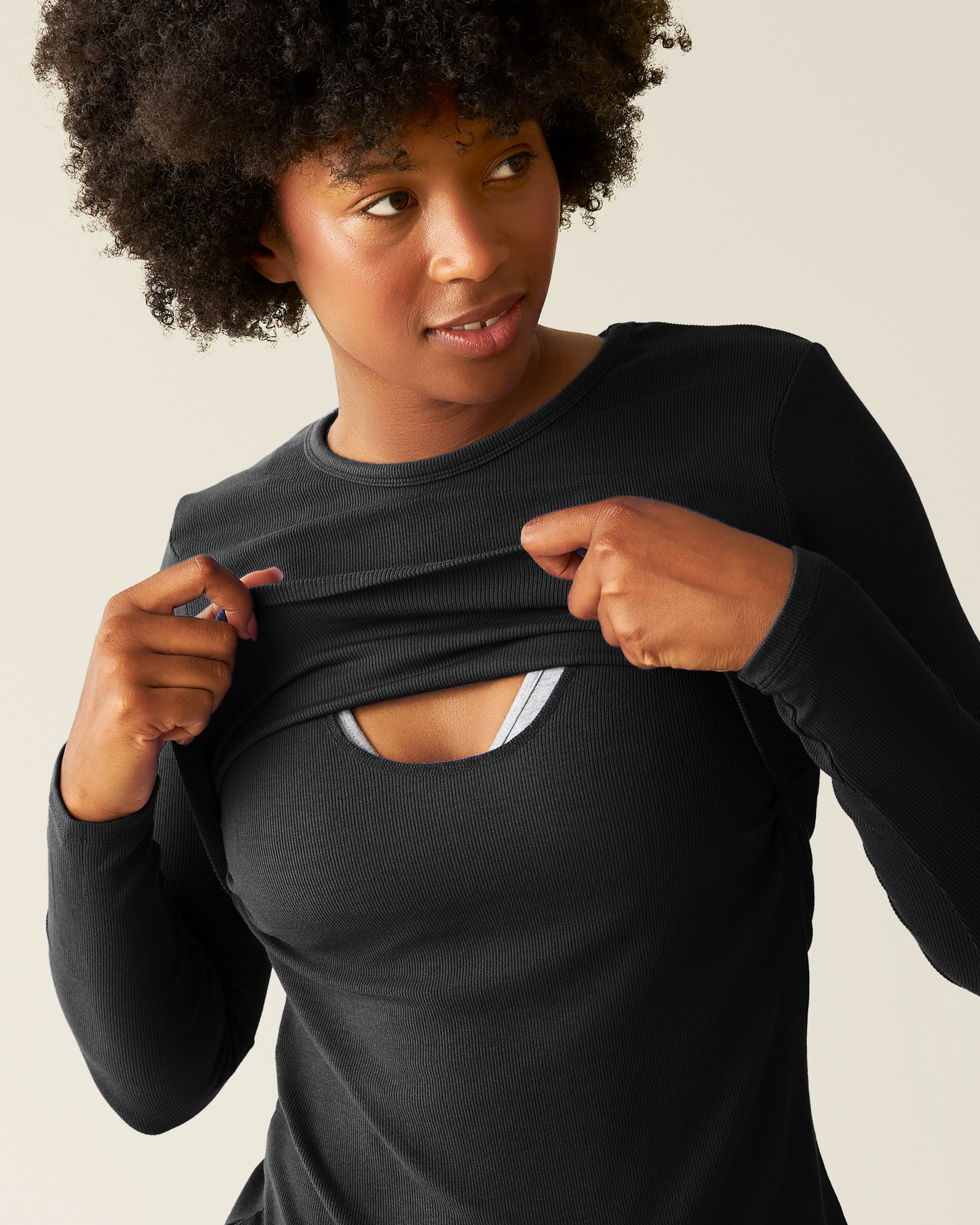 Woman wearing the Ribbed Bamboo Long Sleeve Nursing T-shirt in Black, lifting top outer layer to show nursing access