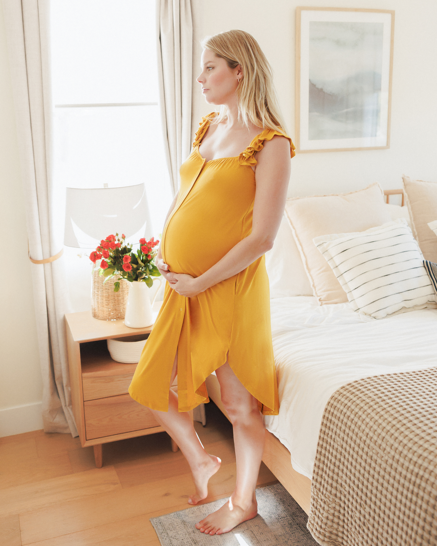 Model standing near bed wearing the Ruffle Strap Labor & Delivery Gown in Honey @model_info:Anna is 5'10" and wearing an XS/S.