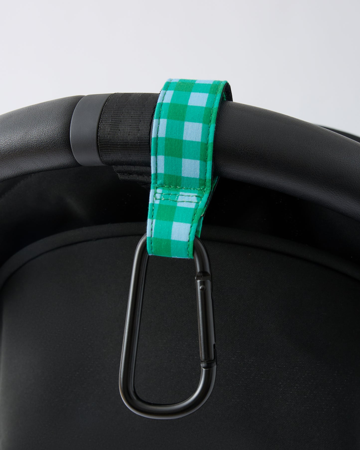 Black stroller handle bar with Stroller Party™ Clips (2-Pack) in Teal Gingham attached, on a beige background.
