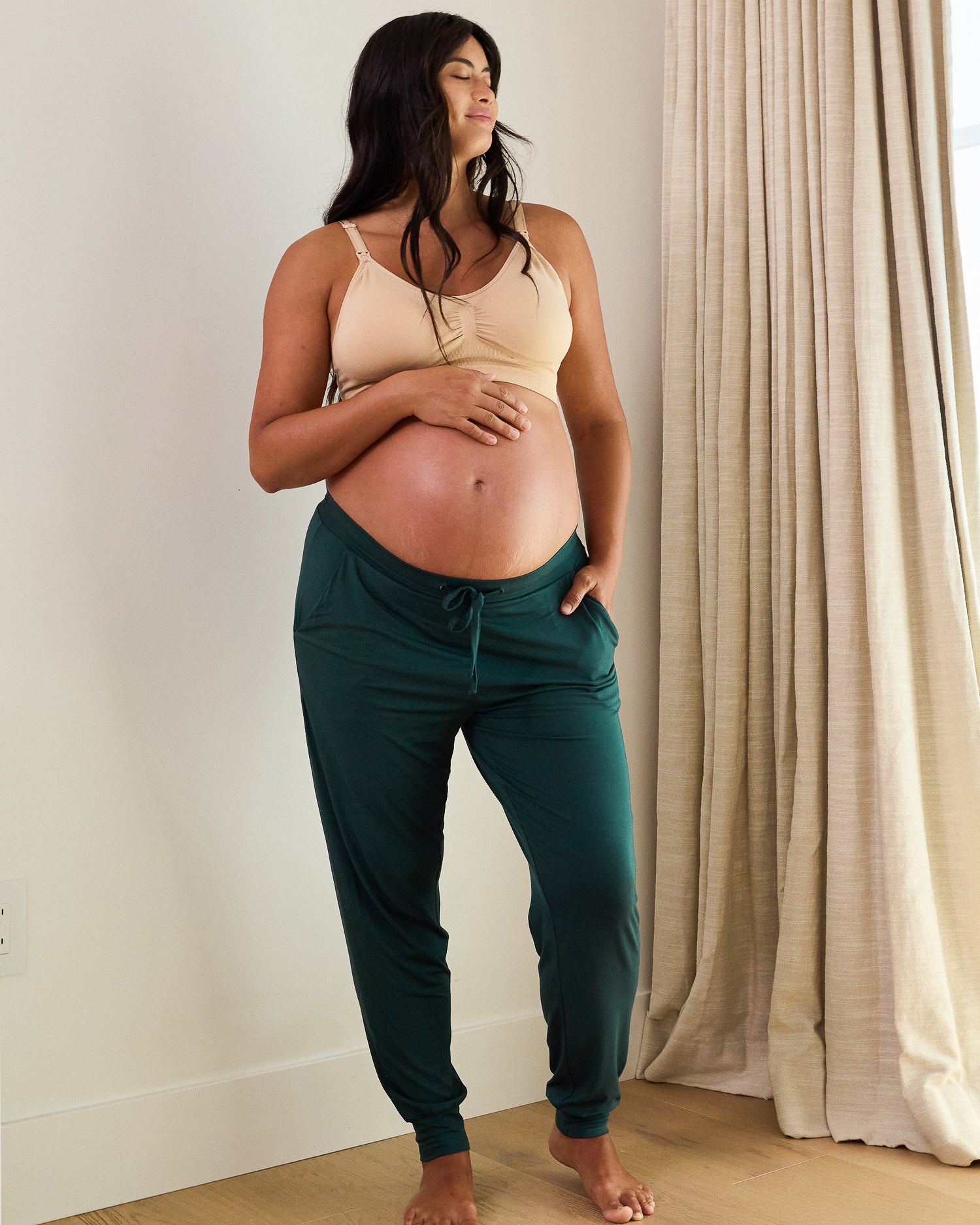 Woman wearing the Everyday Lounge Jogger in evergreen with waistband below belly, paired with a beige bra