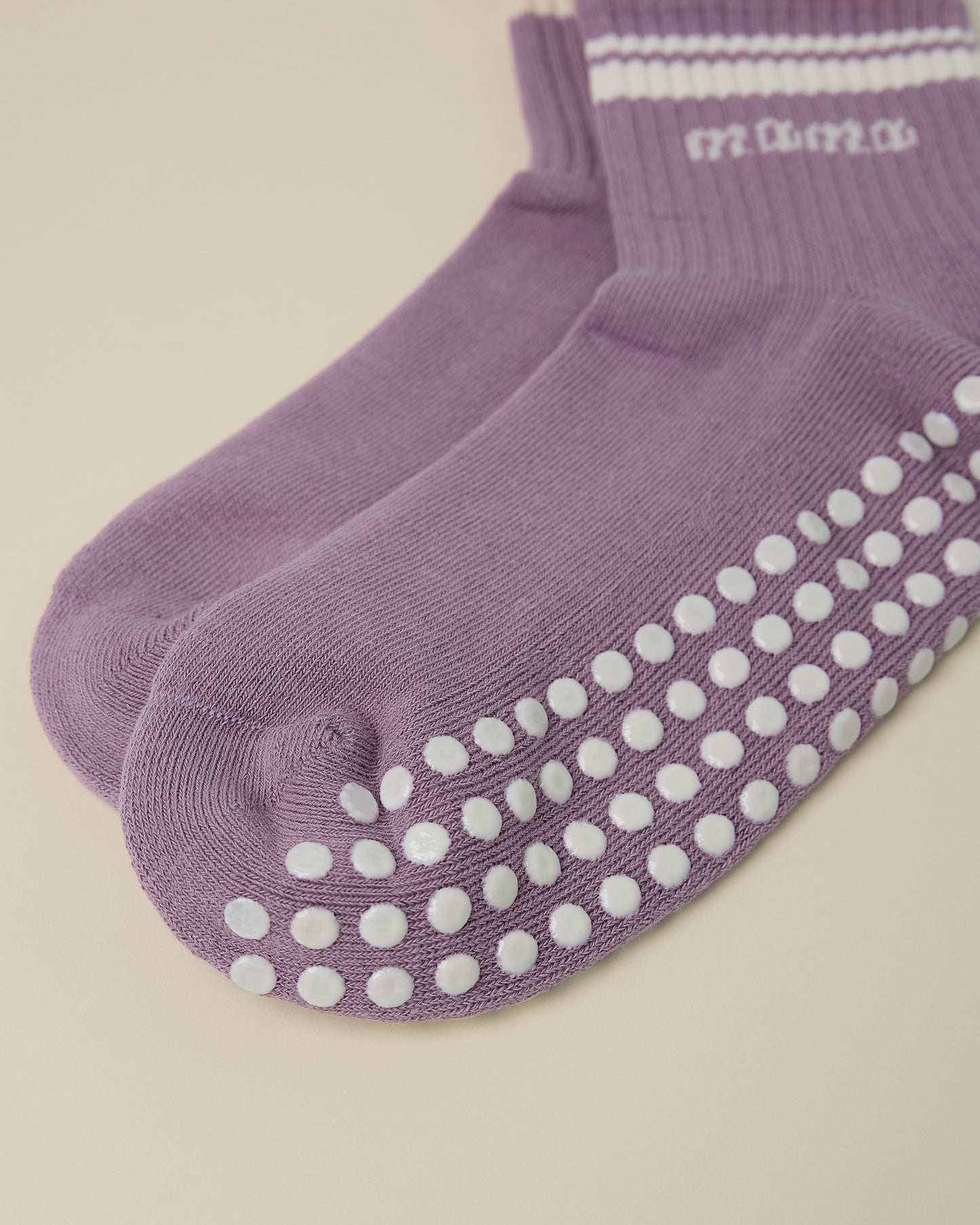 Close up of the non-slip dots on a pair of Non-Slip Quarter Crew Socks in Dusty Mauve & Ivory on a beige background.