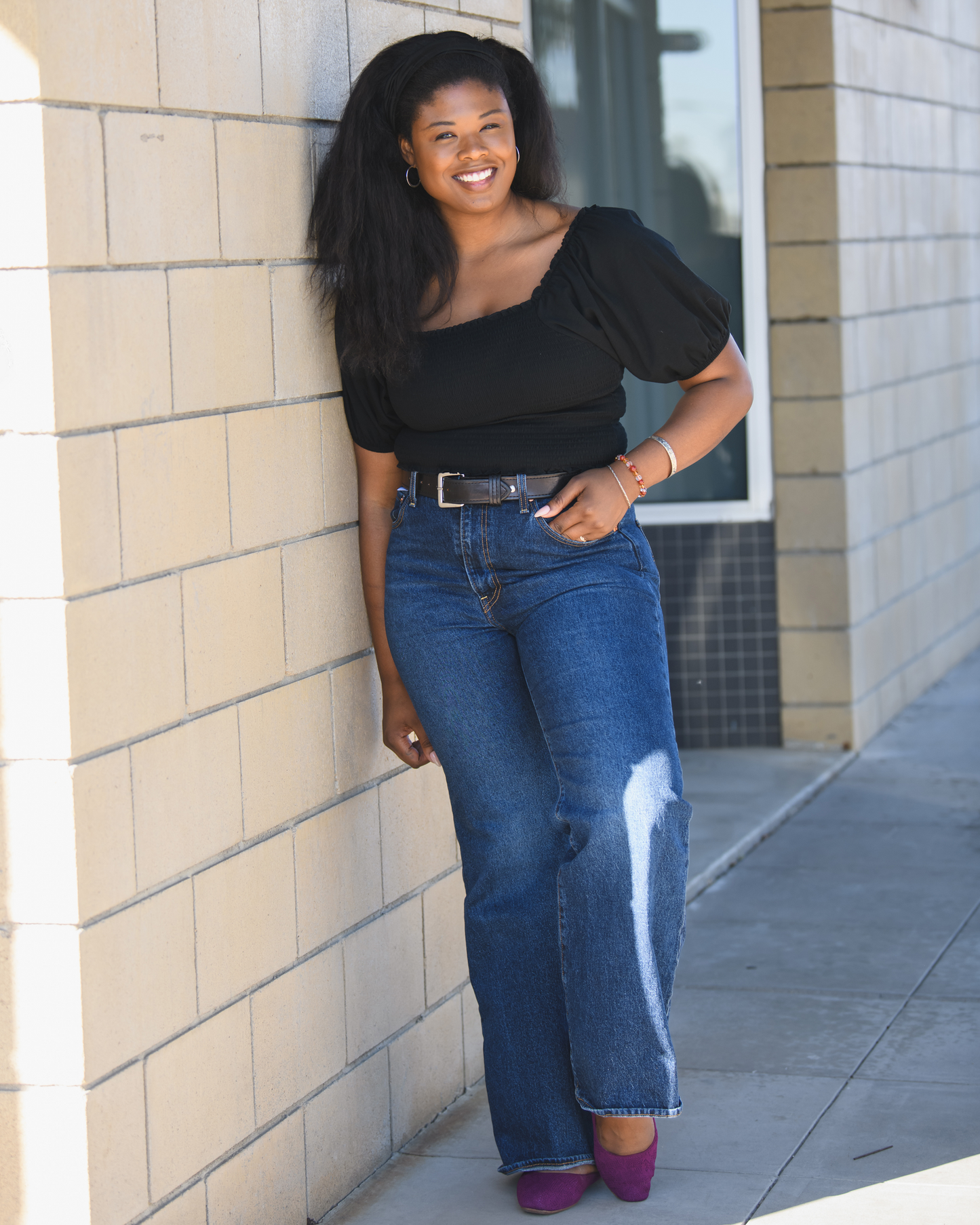 Model outside wearing the Sophia Smocked Cropped Nursing Top in Black, paired with jeans and belt