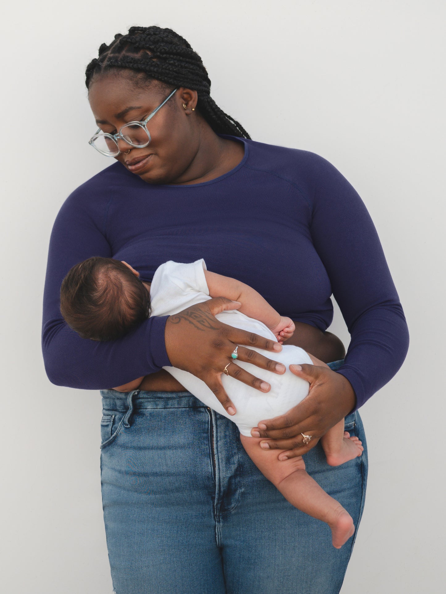 Front view of model nursing baby while wearing the Sublime® Bamboo Maternity & Nursing Cropped Long Sleeve Top in Navy, paired with jeans.