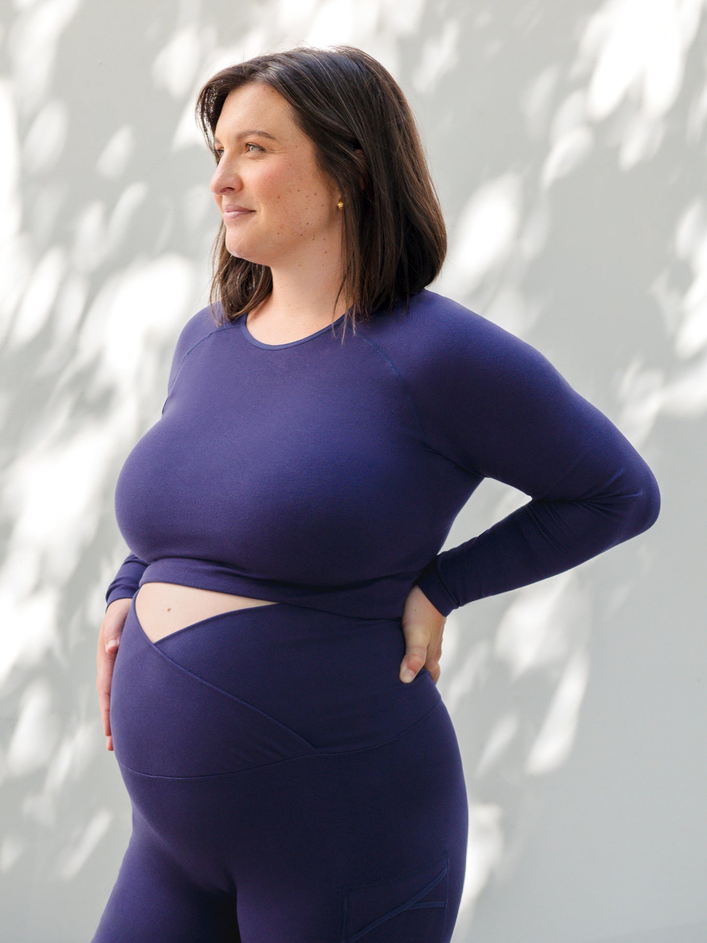 3/4 angle of model standing outside wearing the Sublime® Bamboo Maternity & Nursing Cropped Long Sleeve Top in Navy. @model_info:Shelby is wearing an X-Large.