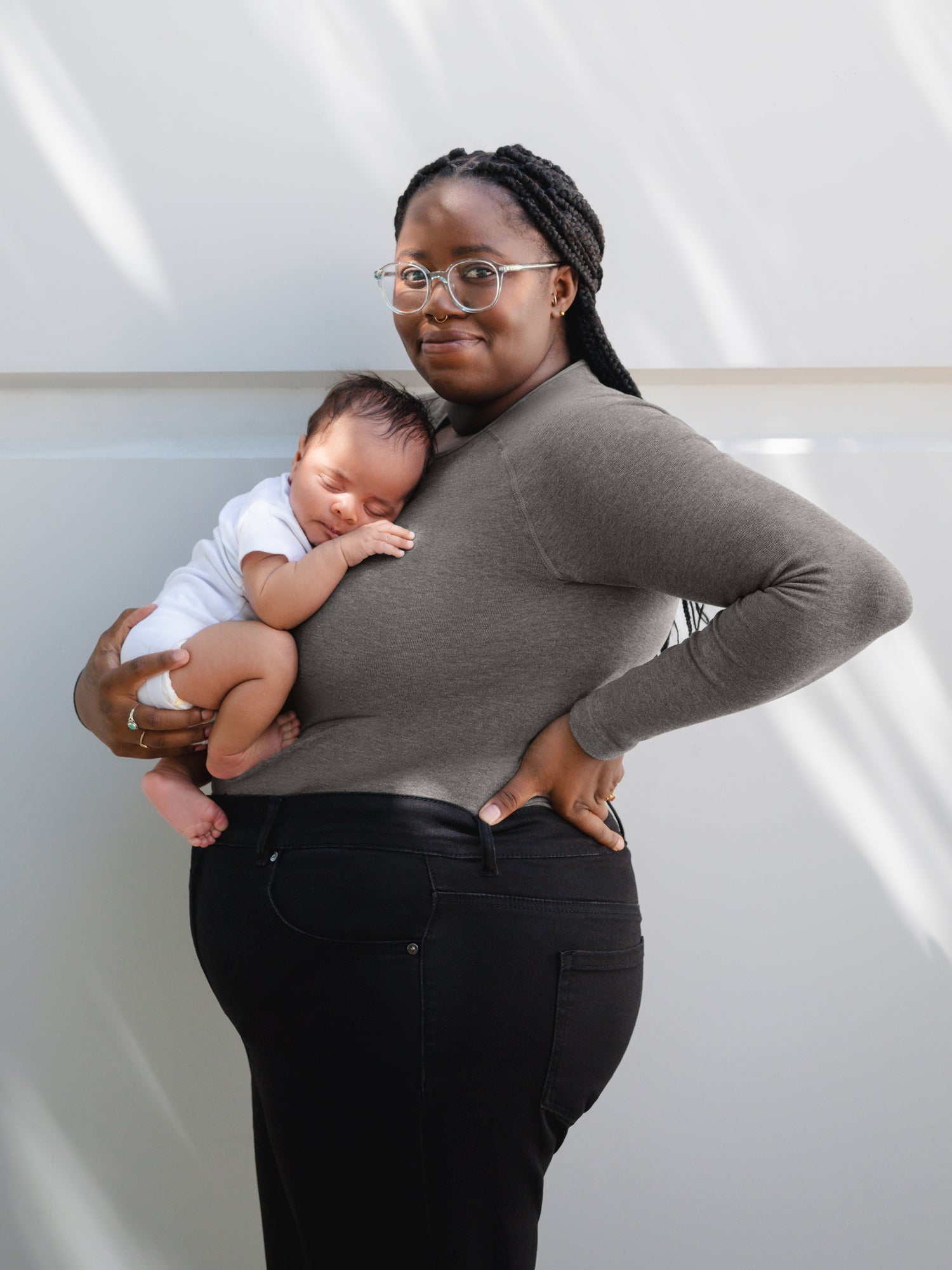 Side view of model wearing the Sublime® Bamboo Maternity & Nursing Cropped Long Sleeve Top in Charcoal, paired with black jeans, and holding baby. @model_info:Leondra is wearing a 1X Busty.