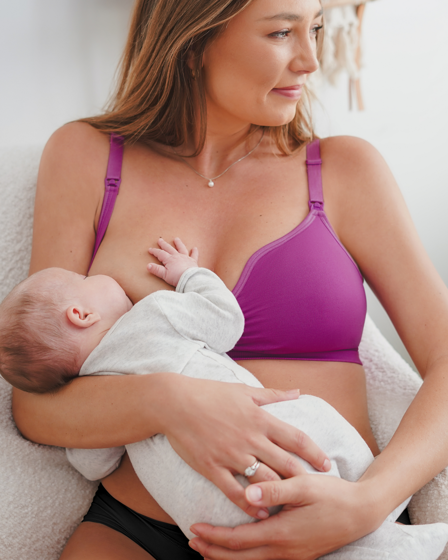 Model sitting wearing the Tatum Seamless Maternity & Nursing Bralette in Orchid, and nursing baby.