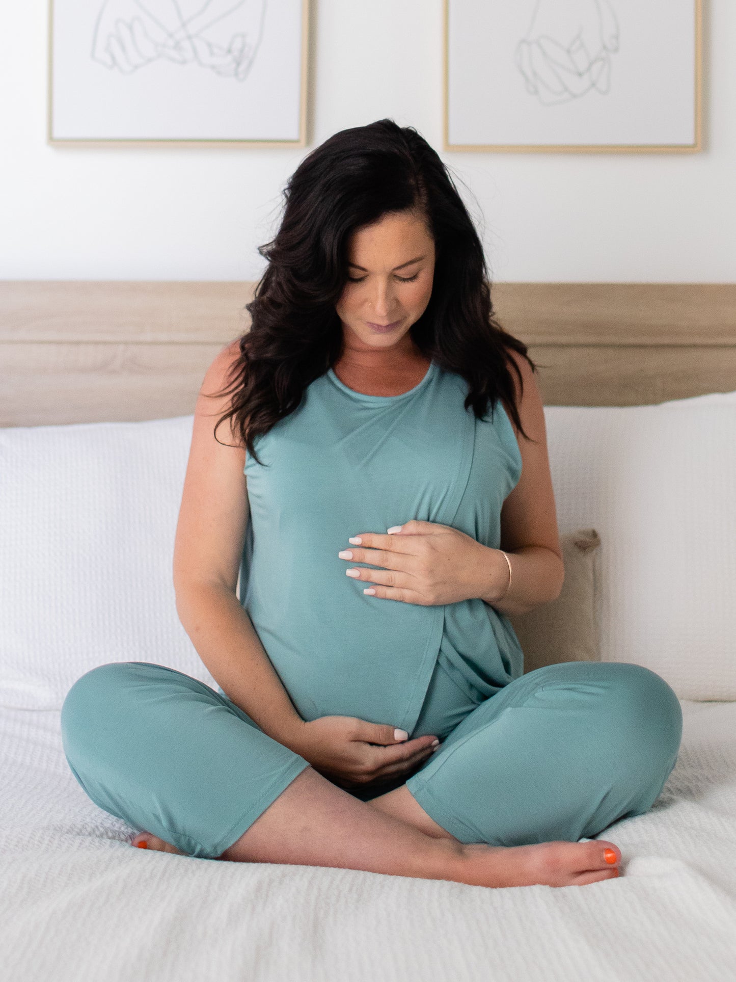 Front view of pregnant model sitting cross-legged on bed wearing the Tulip Hem Nursing Tank & Capri Pajama Set in Aqua. @model_info:Alicia is wearing a Medium.