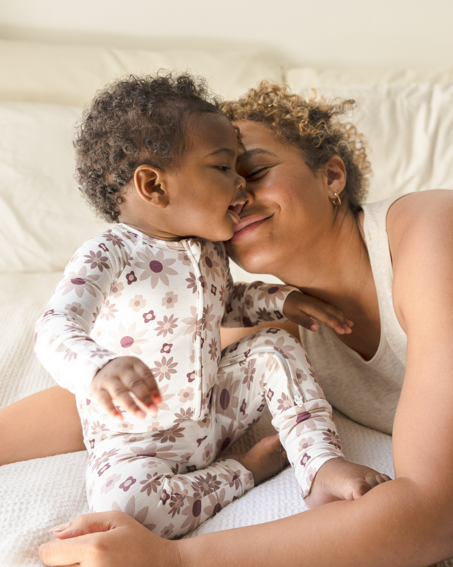Child wearing Bamboo Baby Pajamas in Twilight Floral while lying on a bed with her Mom, smiling.